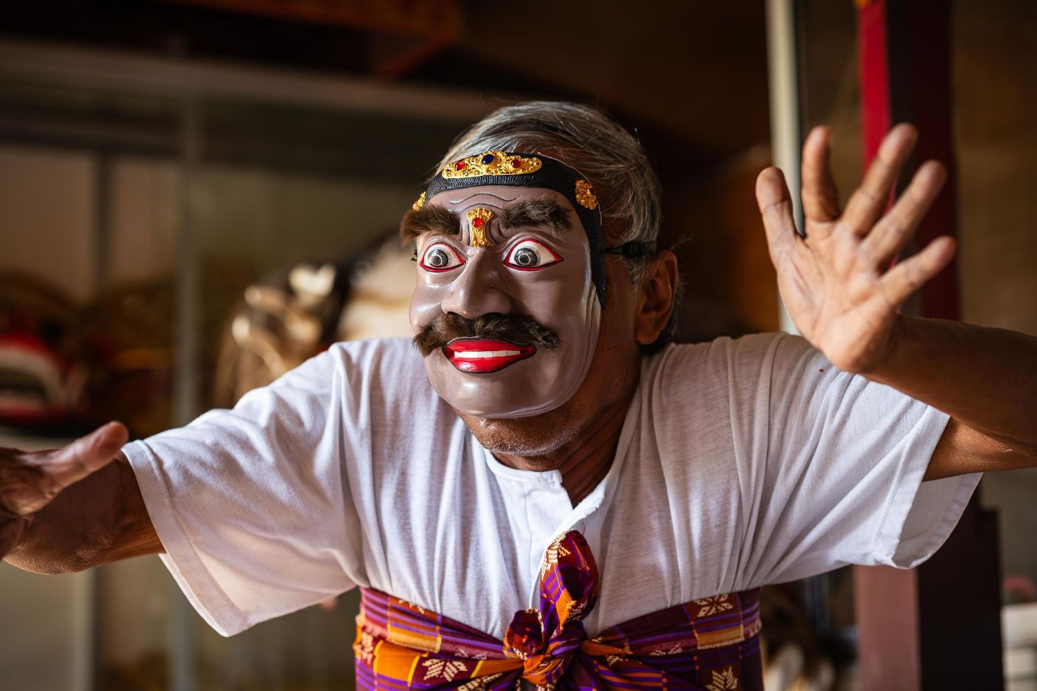 Traditional Indonesian carver wearing a minister's mask and white t-shirt gestures expressively during cultural performance.