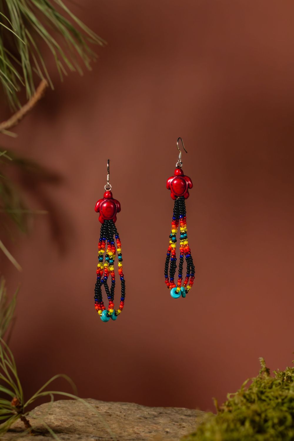 Colorful beaded dangle earrings with red turtle tops and multicolored glass beads featuring orange, turquoise and black tones.