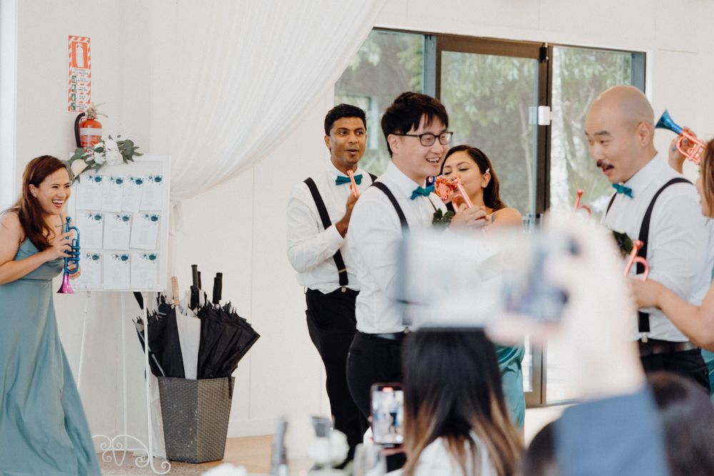 Wedding party members dressed in teal and black raise champagne bottles captured by Apertured Media Auckland Wedding Photographer.