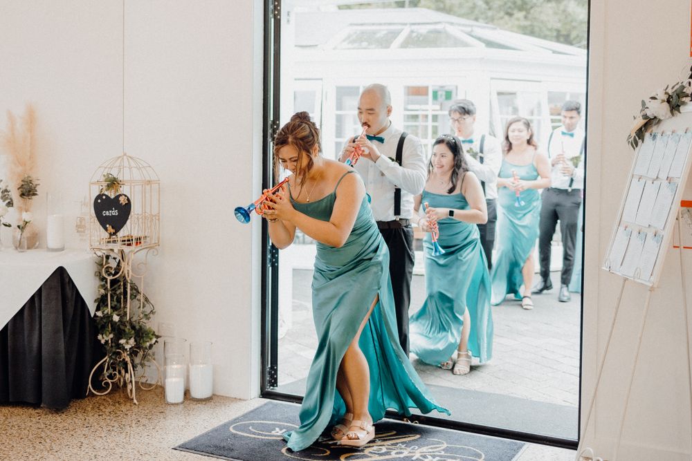 Wedding party members in turquoise dresses make a joyful entrance captured by Apertured Media Auckland Wedding Photographer.
