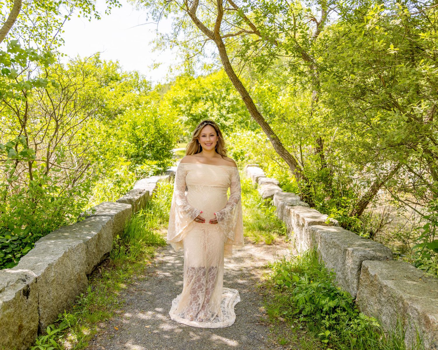 Sunlit stone path through green garden with elegant figure in lace dress.
