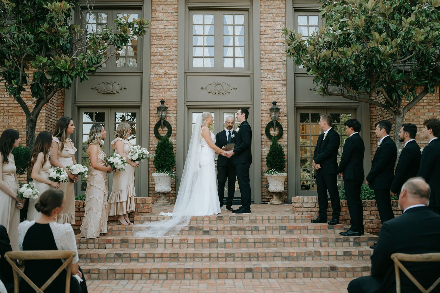 Wedding ceremony taking place on elegant brick steps with attendants lined up on both sides. Estate wedding in Texas.