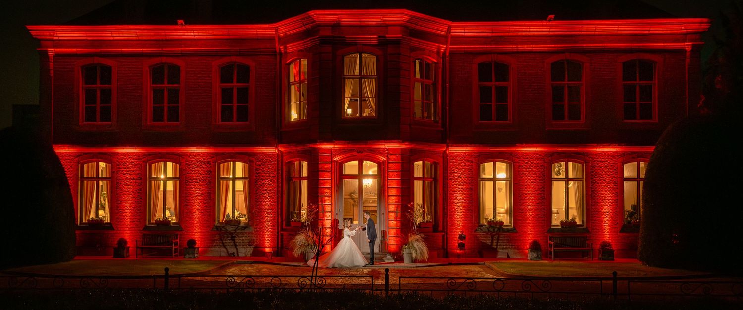 Grande demeure illuminée par une lumière rouge spectaculaire lors d’une réception de mariage en soirée.