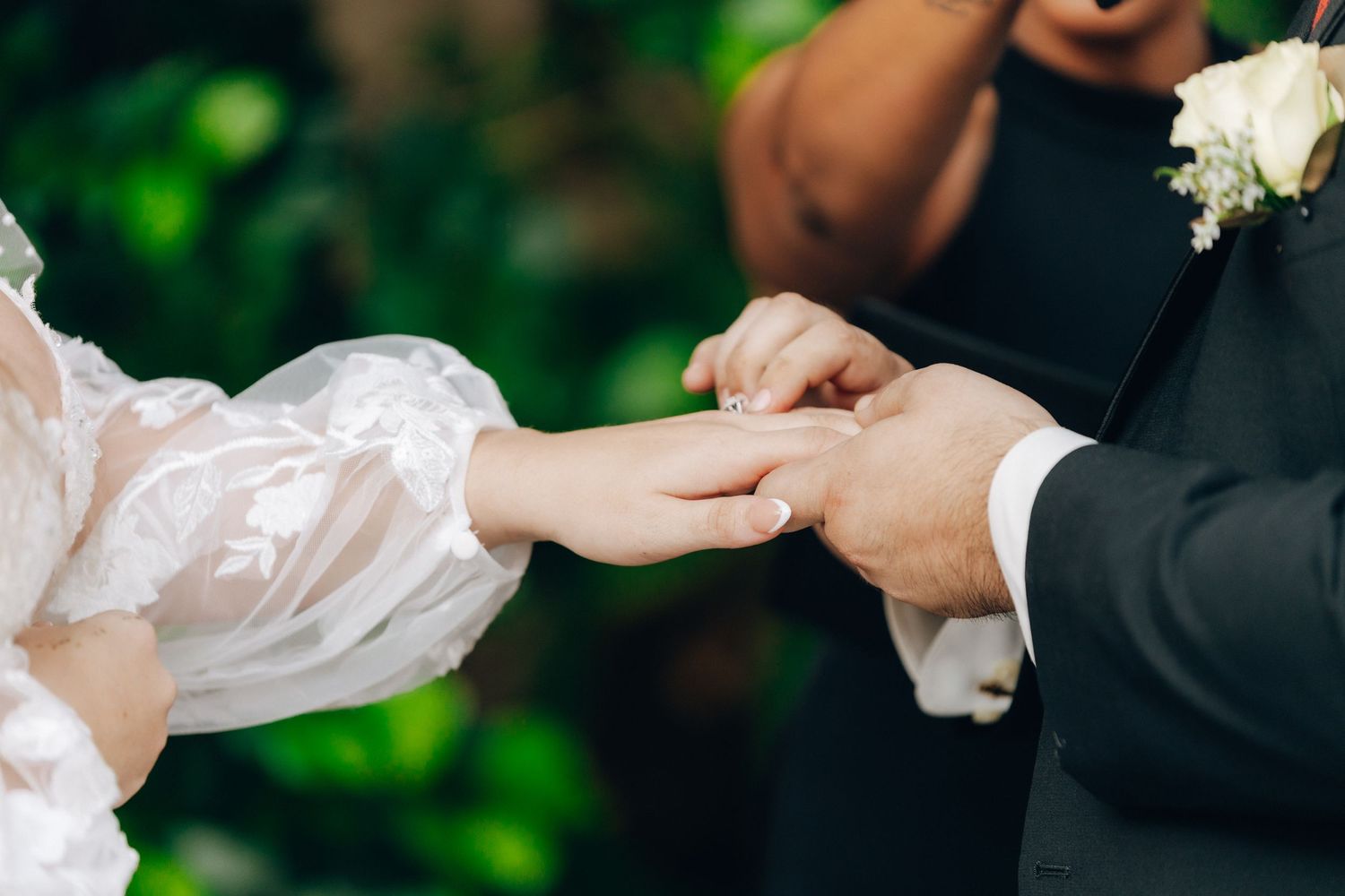 Close-up of hands exchanging rings during an outdoor wedding ceremony.