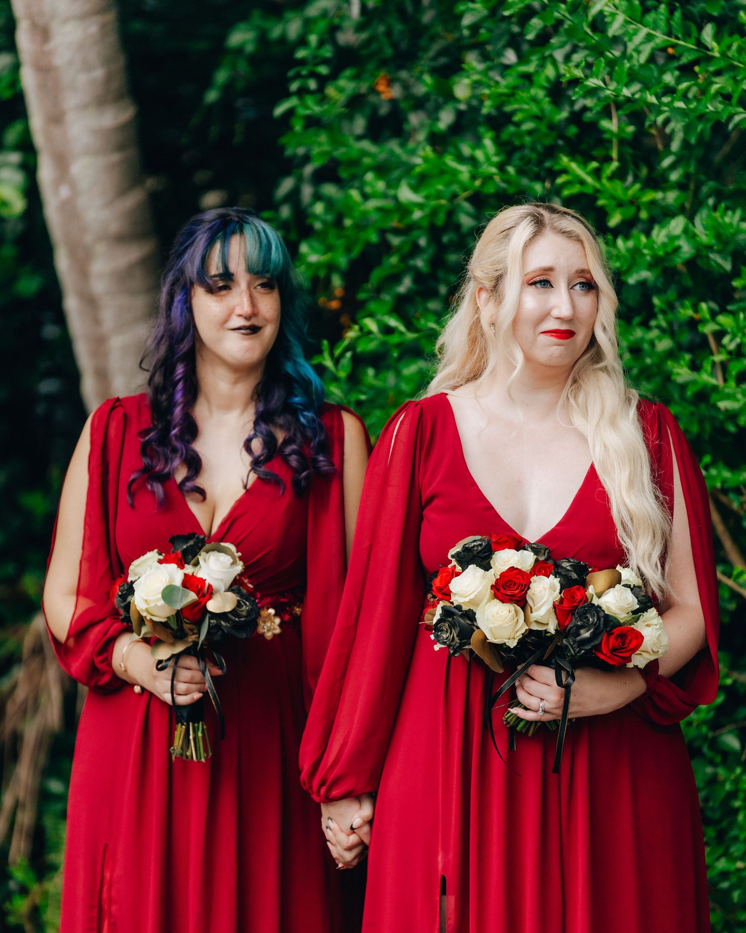 Two bridesmaids in matching red dresses hold white and red bouquets.