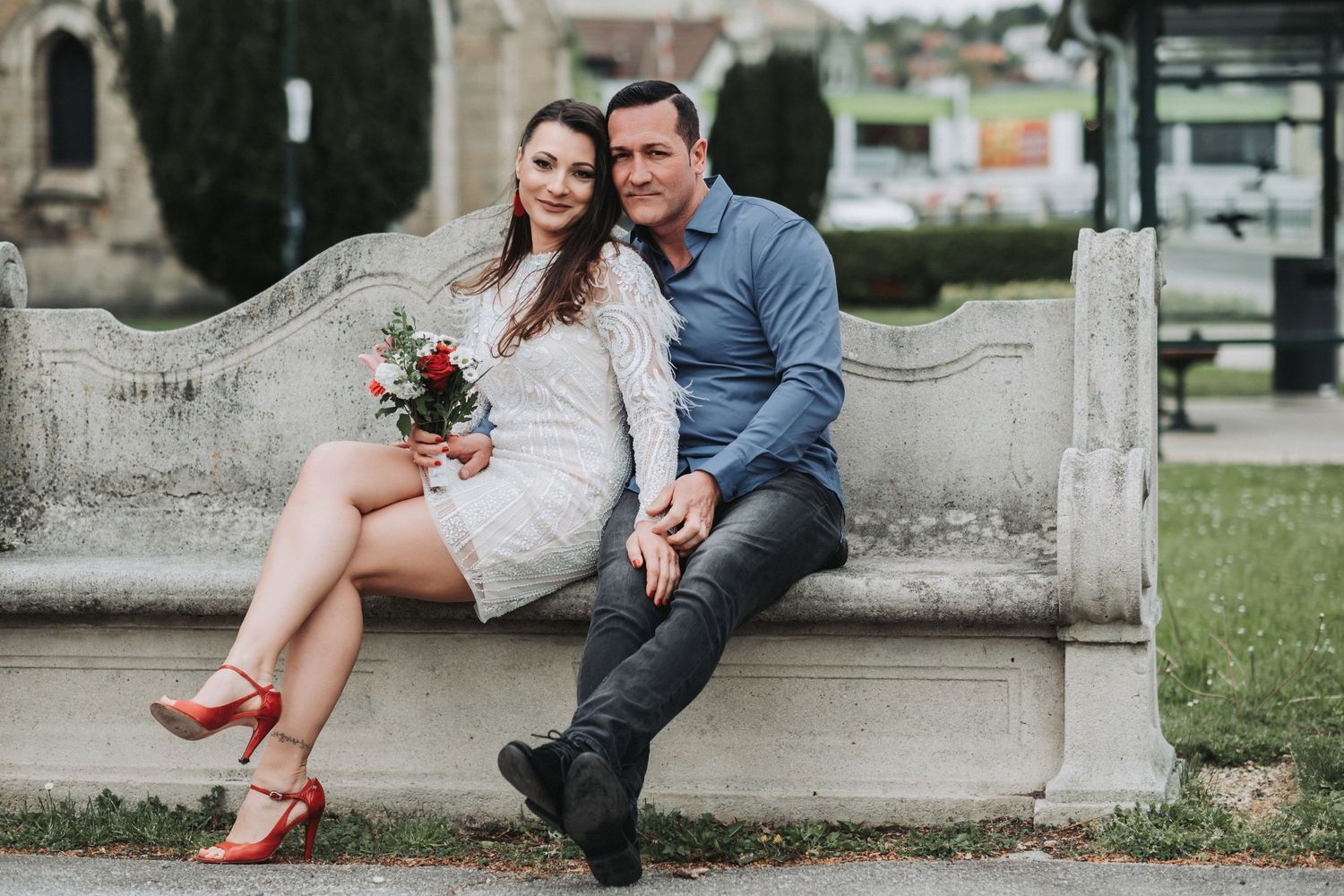 A couple shares a tender moment on stone steps with the woman in white lace dress and red heels.