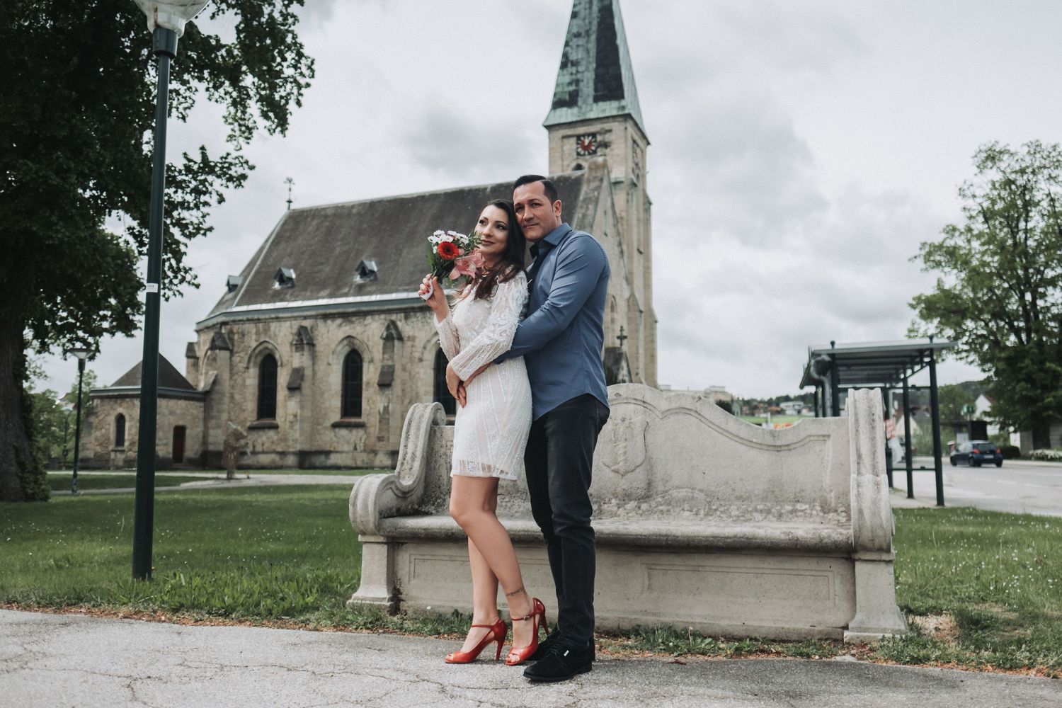 A couple poses together in front of a historic church with a tall spire in the background.