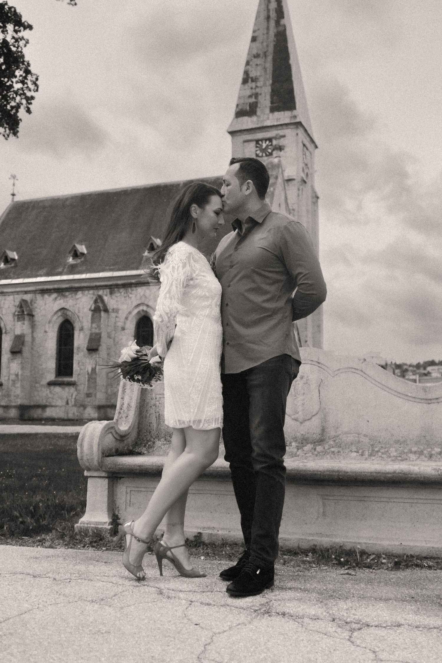 A black and white romantic photo of a couple embracing in front of a church spire.