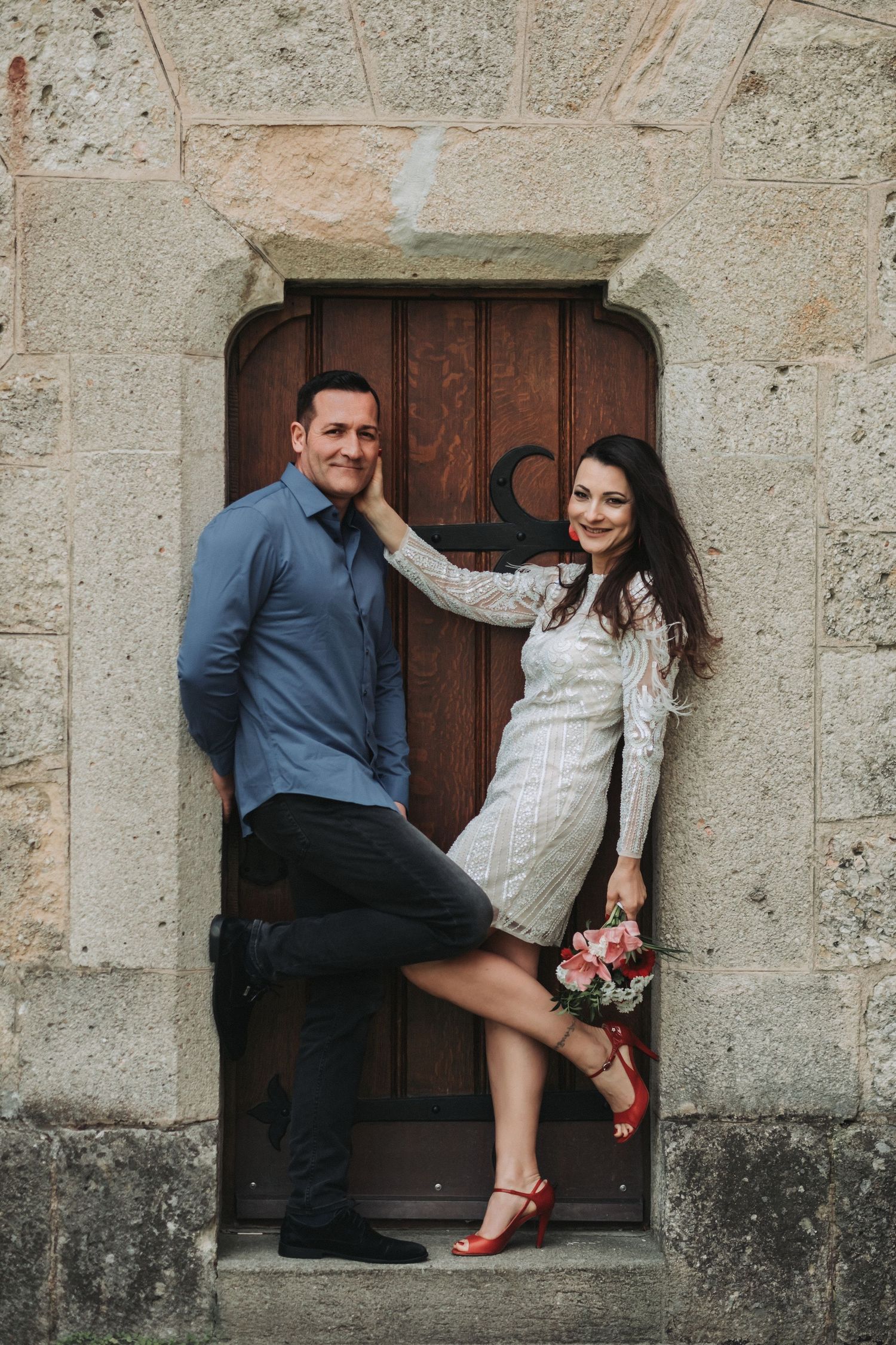 A couple poses in a rustic doorway framed by stone architecture.