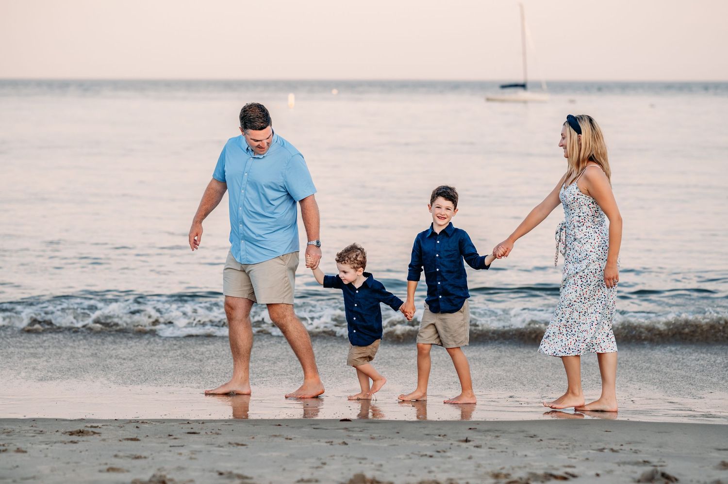 Family walking together holding hands along a sandy beach at sunset with ocean in the background.