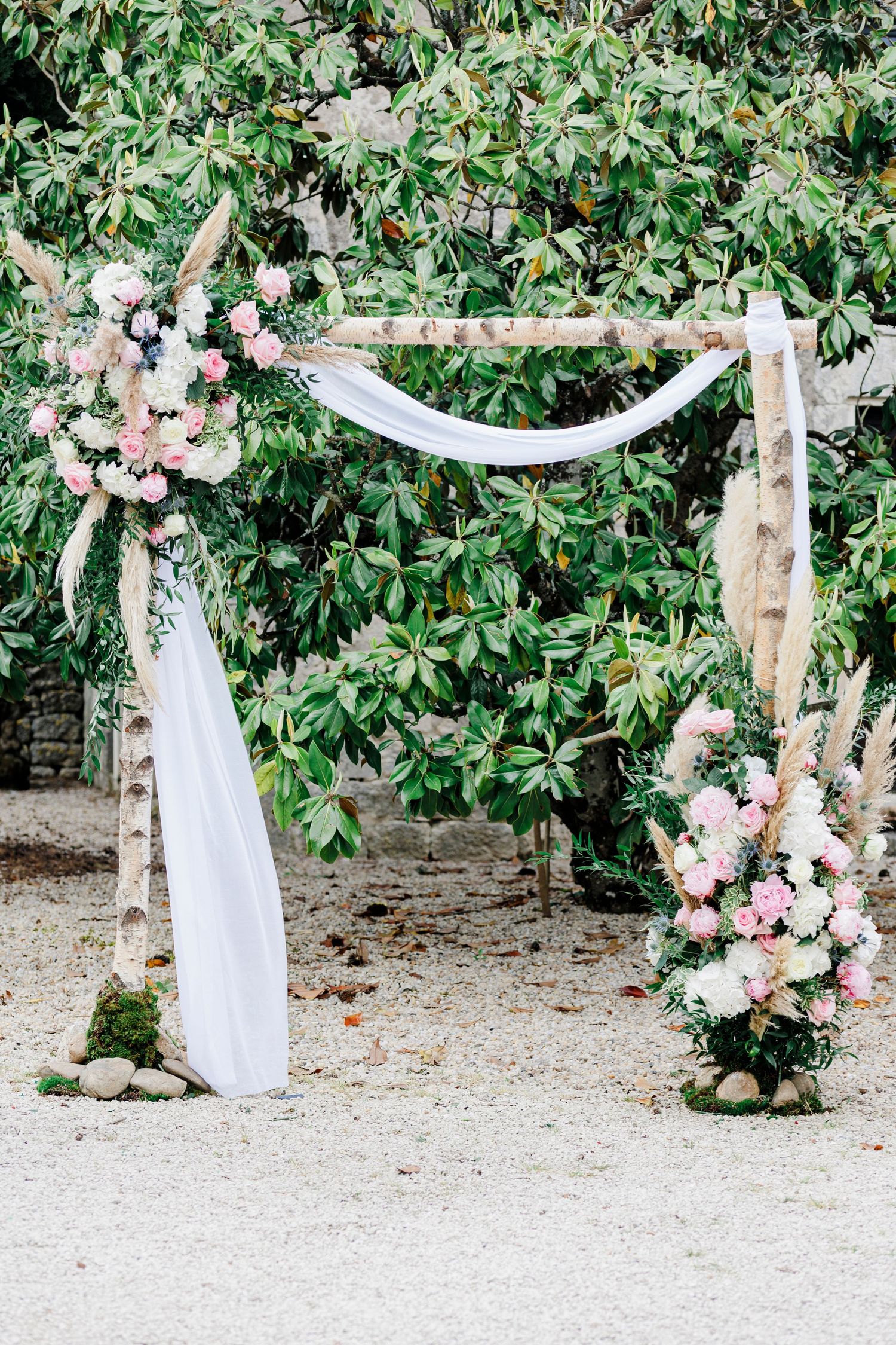 Romantic outdoor wedding arch decorated with flowing white fabric, pampas grass, blush pink and white flowers at Domaine des Gaillardoux