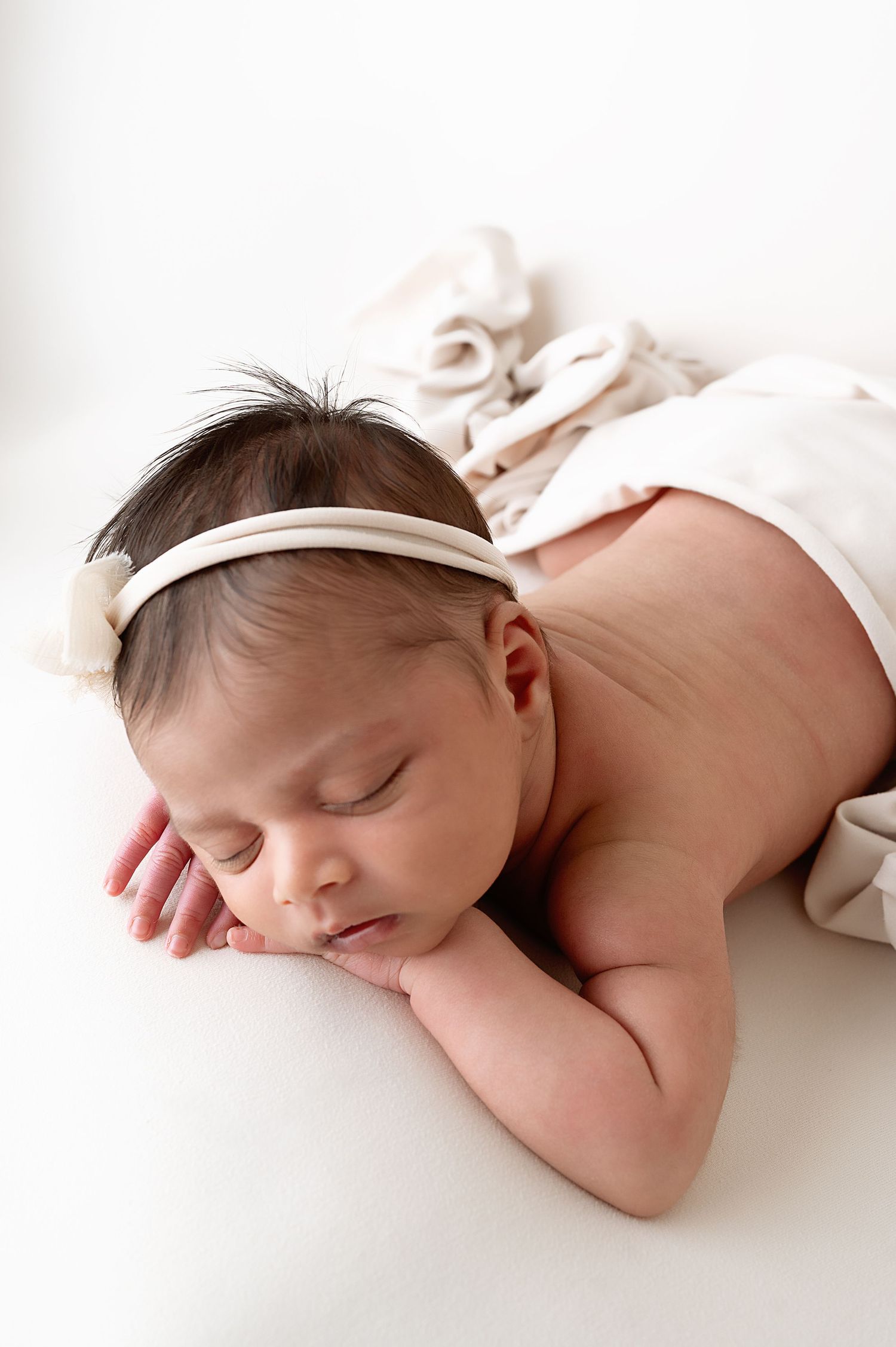 Sleeping newborn wearing white headband on white blanket.