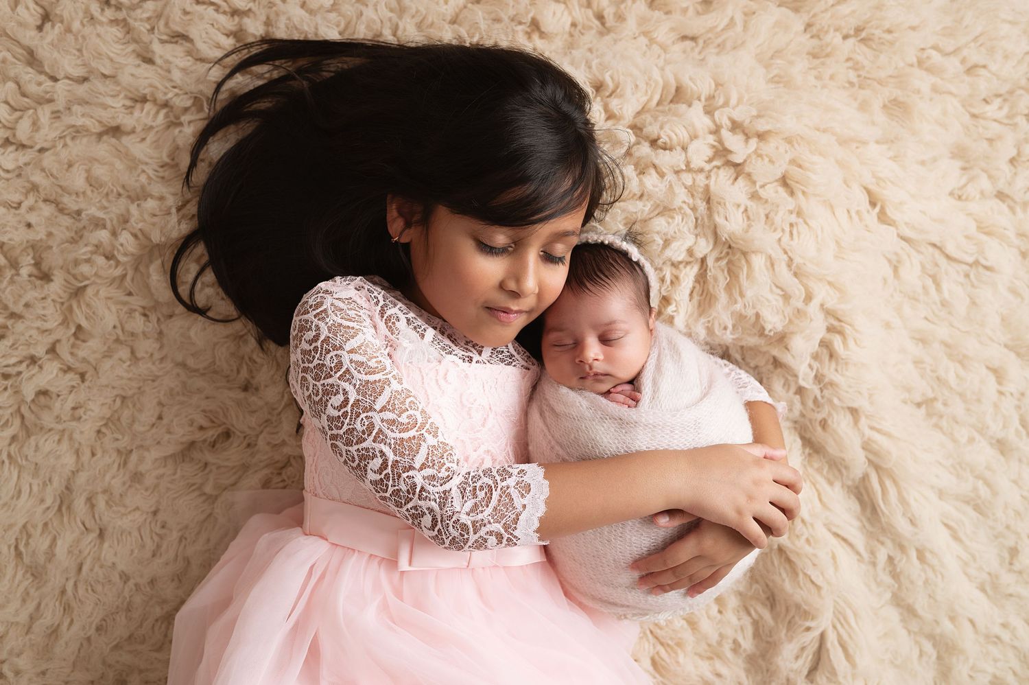 Mother and baby laying on beige textured carpet during photo session.