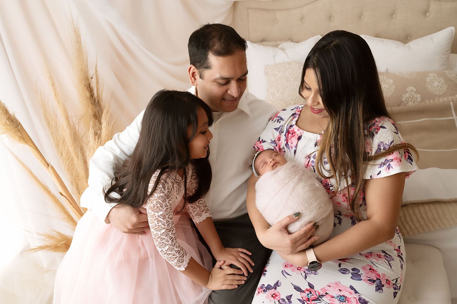 Family sharing intimate moment with newborn on beige upholstered headboard.