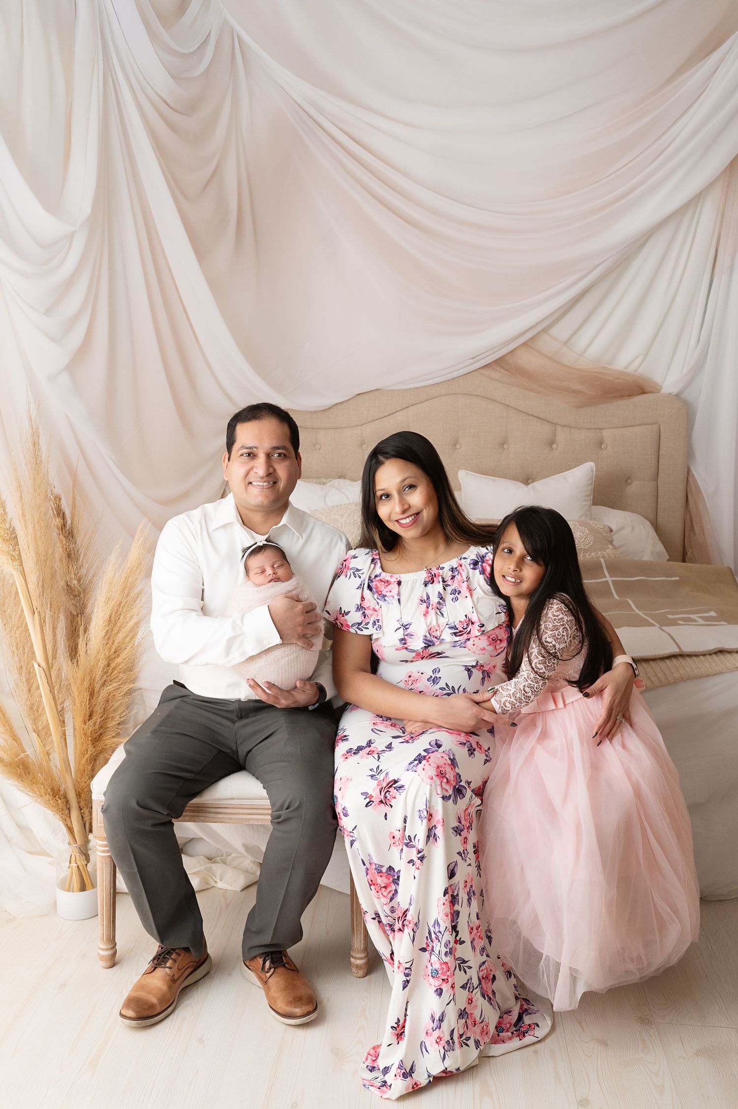 Family portrait in front of white draped backdrop with pampas grass decor.
