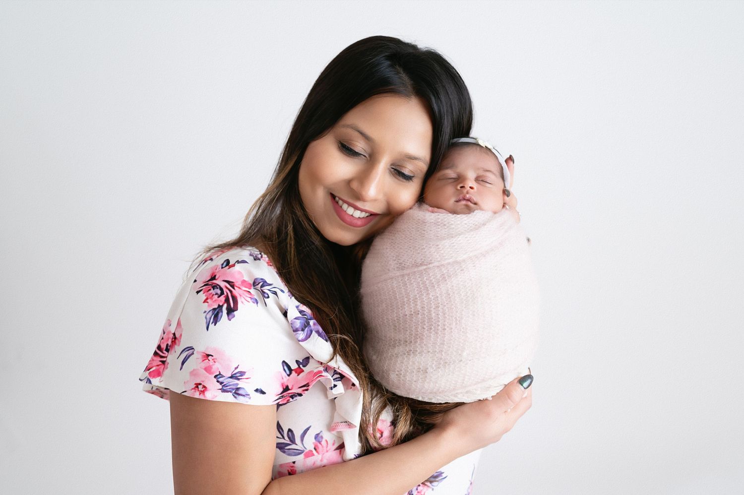 Mother in floral dress holding swaddled newborn during portrait session.