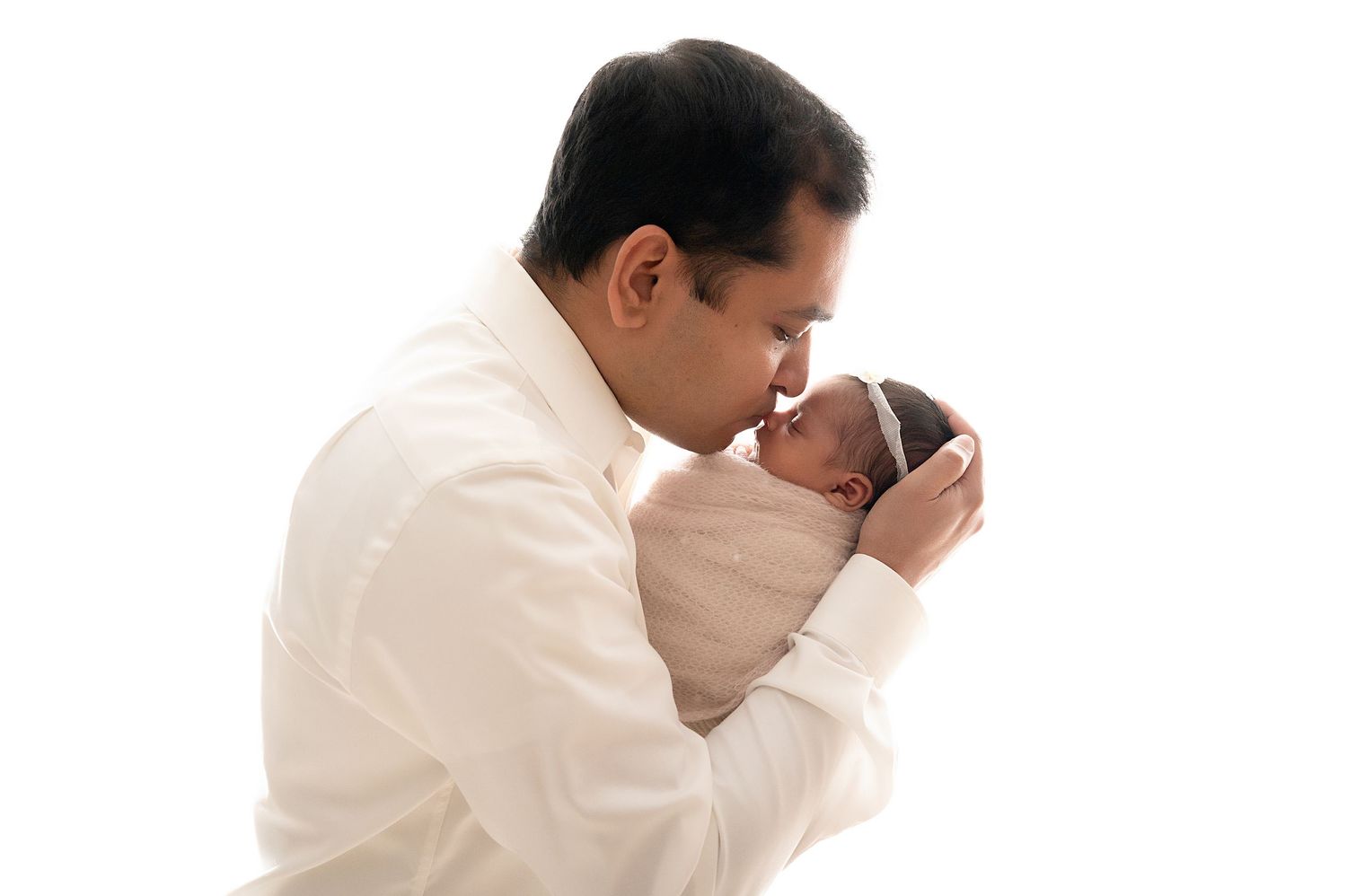 Tender moment between father and newborn against white background.