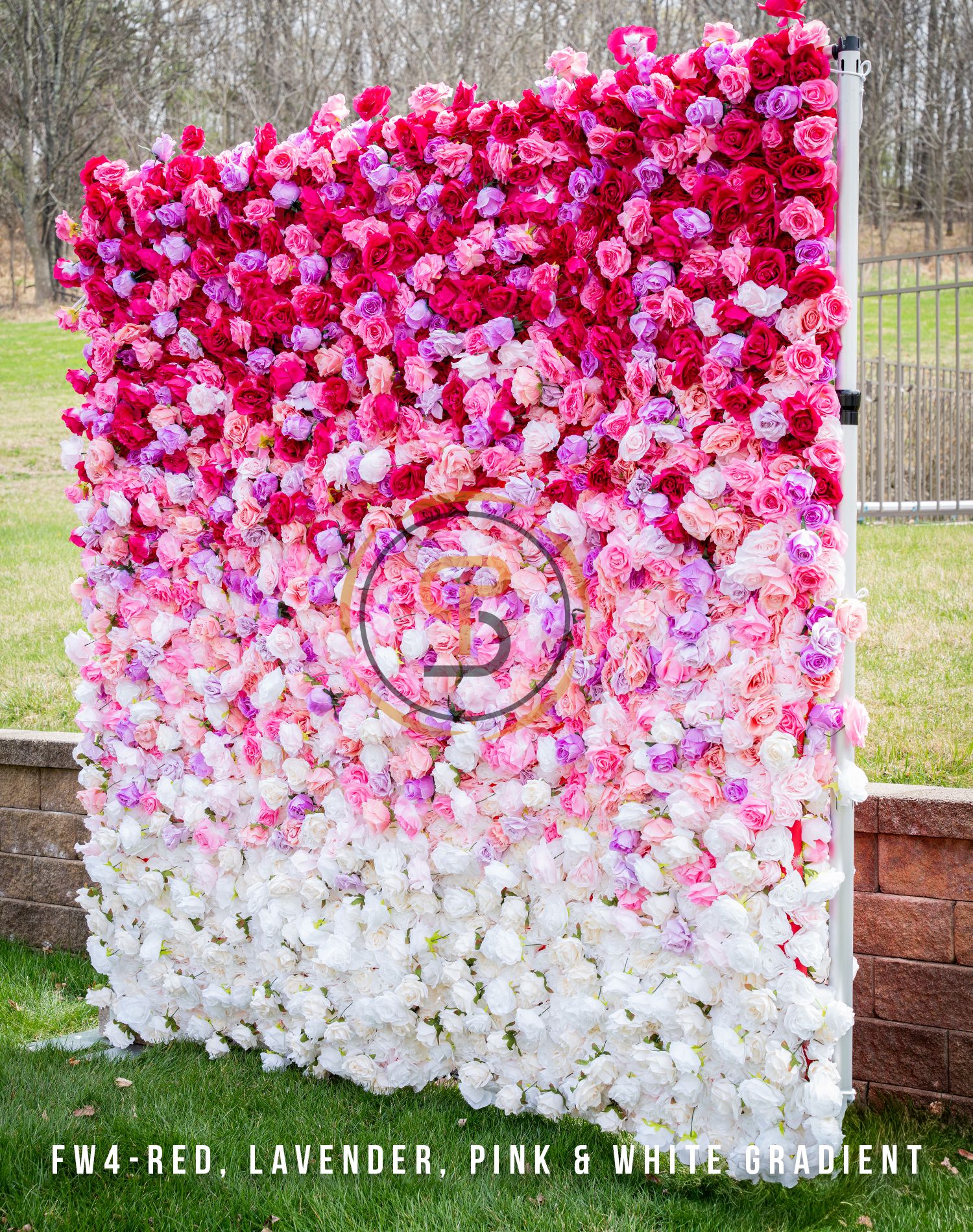 Stunning ombre flower wall transitioning from red to pink to white with centered circular emblem.