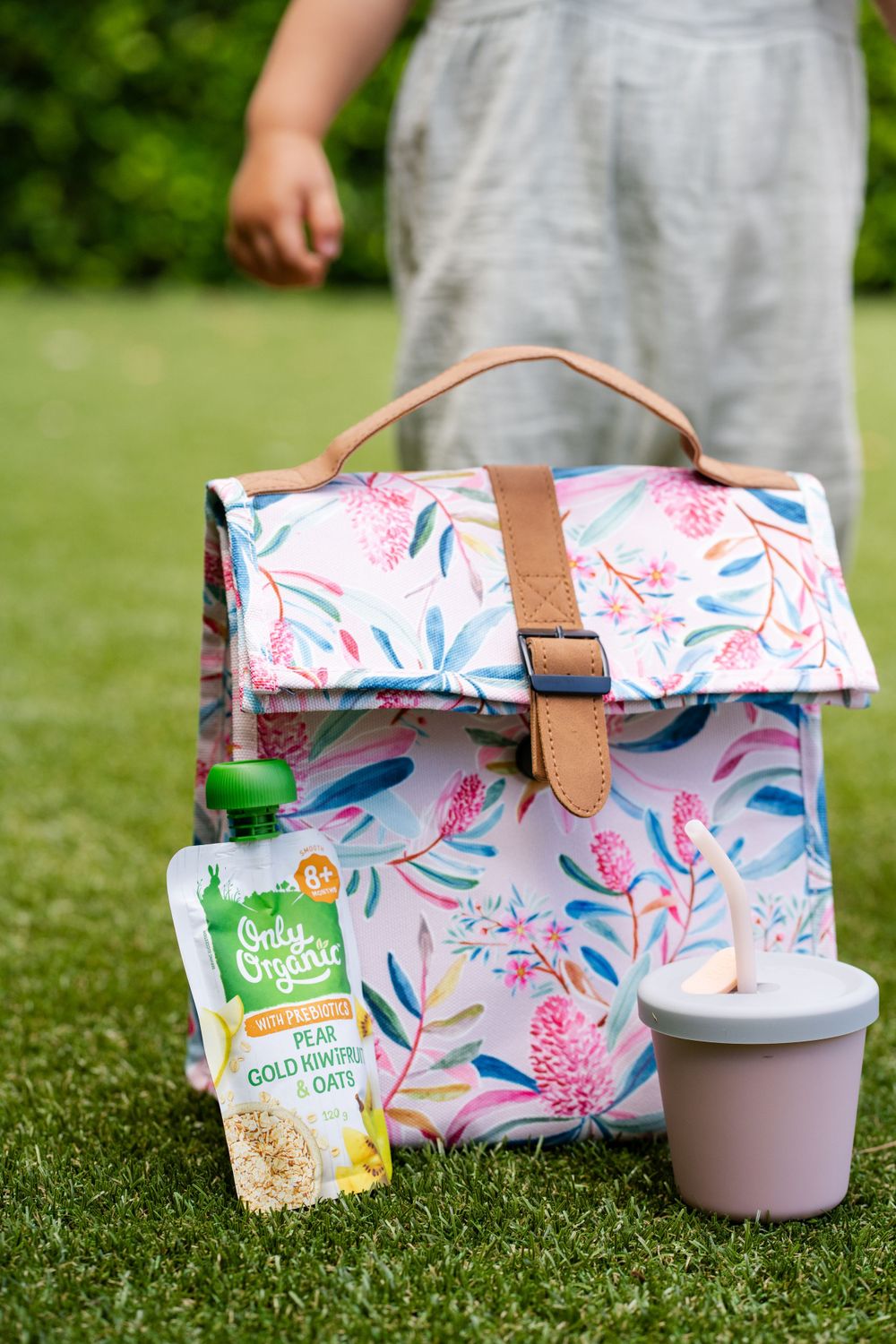 Floral print lunch bag with organic snack pouch and cup on grass outdoors.