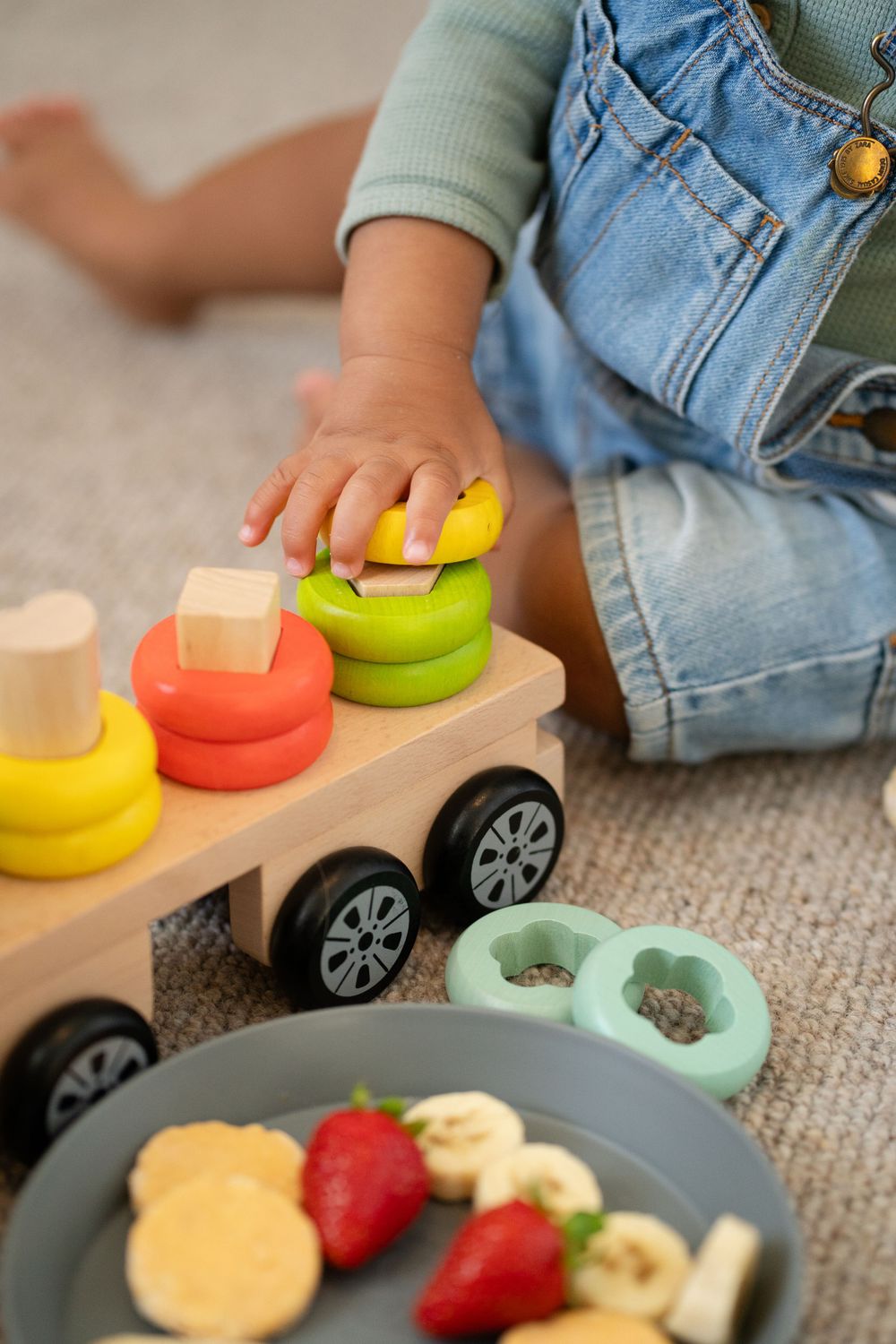 Close up of child playing with colorful wooden stacking toy next to plate of fresh fruit.