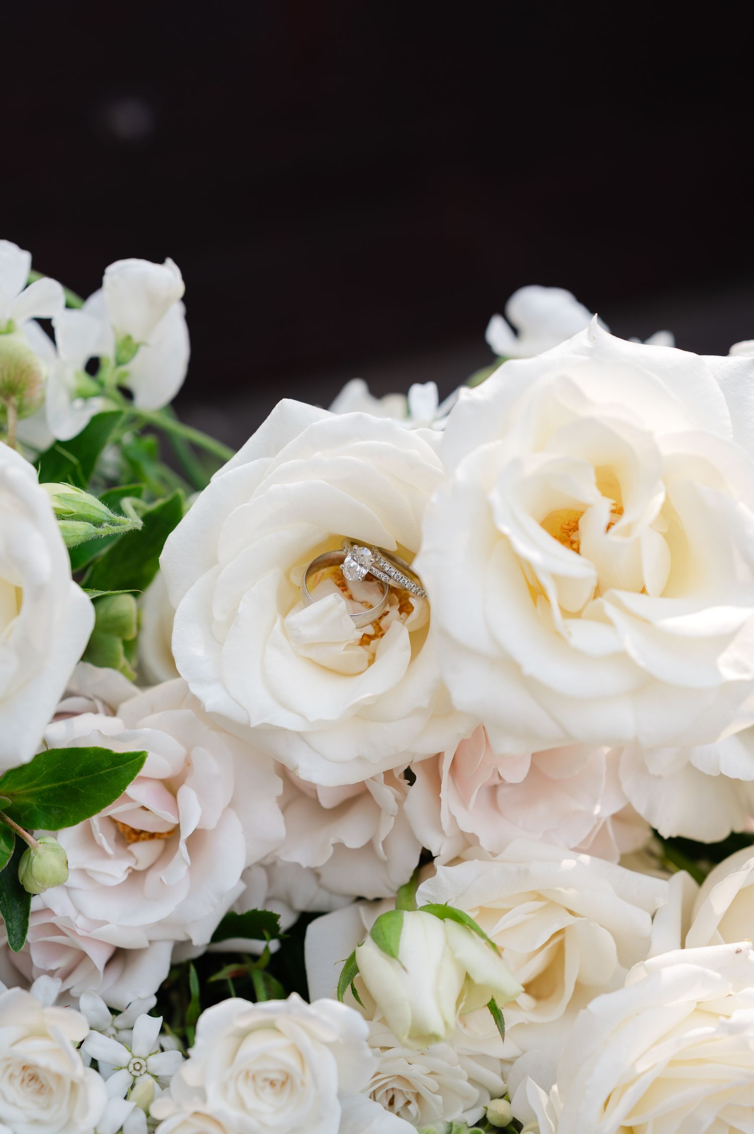 Wedding rings nestled beautifully in white roses surrounded by a romantic floral arrangement.