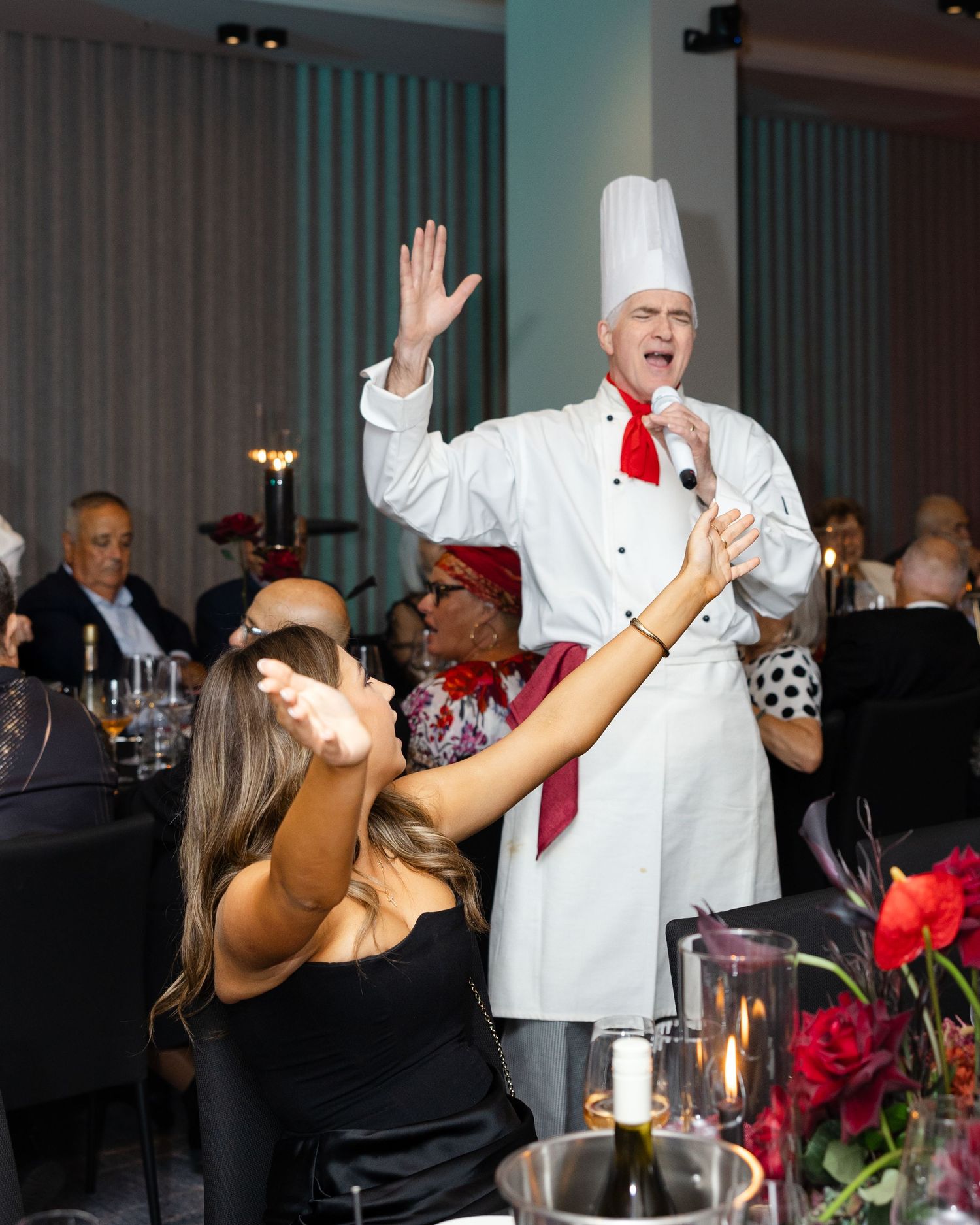 Chef in traditional white uniform and red tie entertaining guests during an elegant dining event.