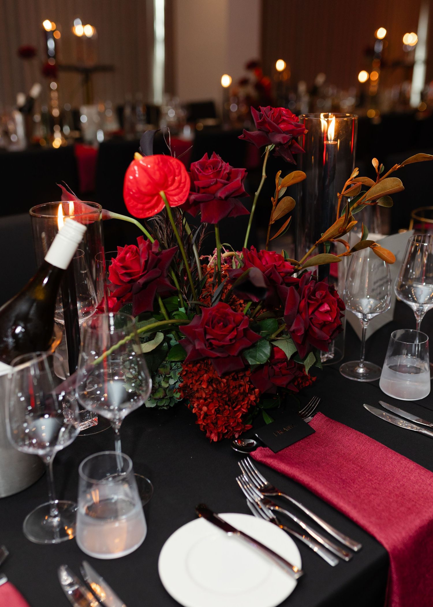 Elegant table setting featuring black tablecloth, burgundy napkins, and deep red roses in a romantic dinner arrangement.