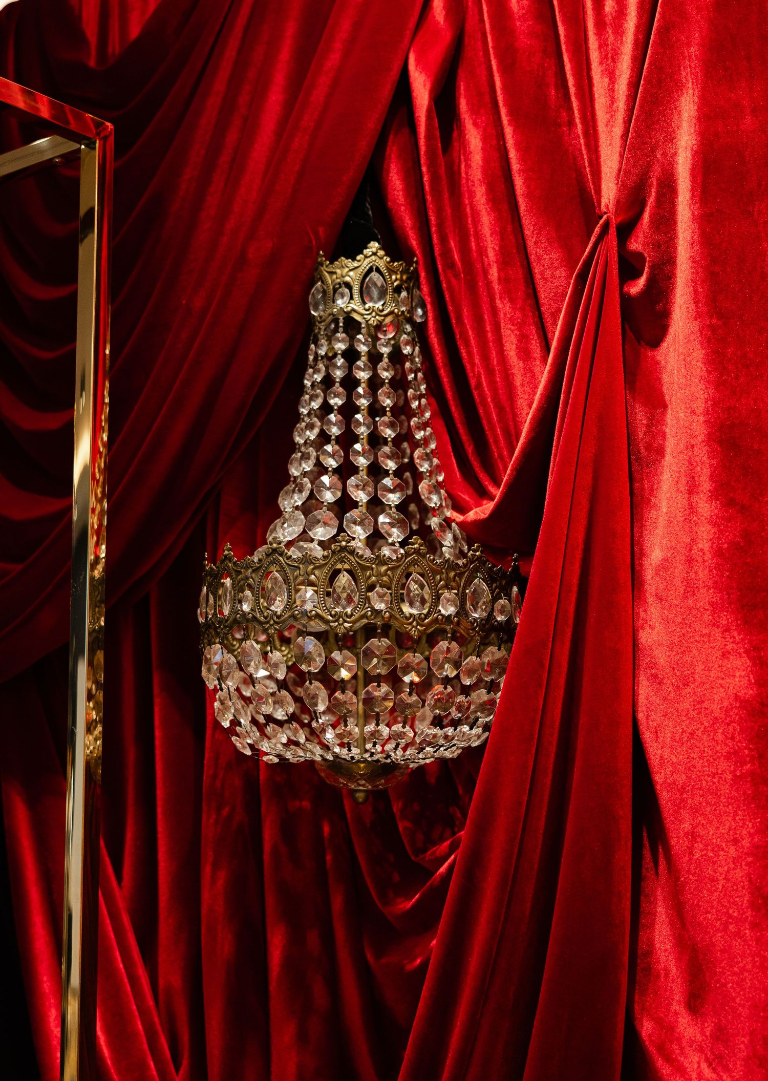 A vintage crystal chandelier hangs in front of luxurious red velvet theater curtains.