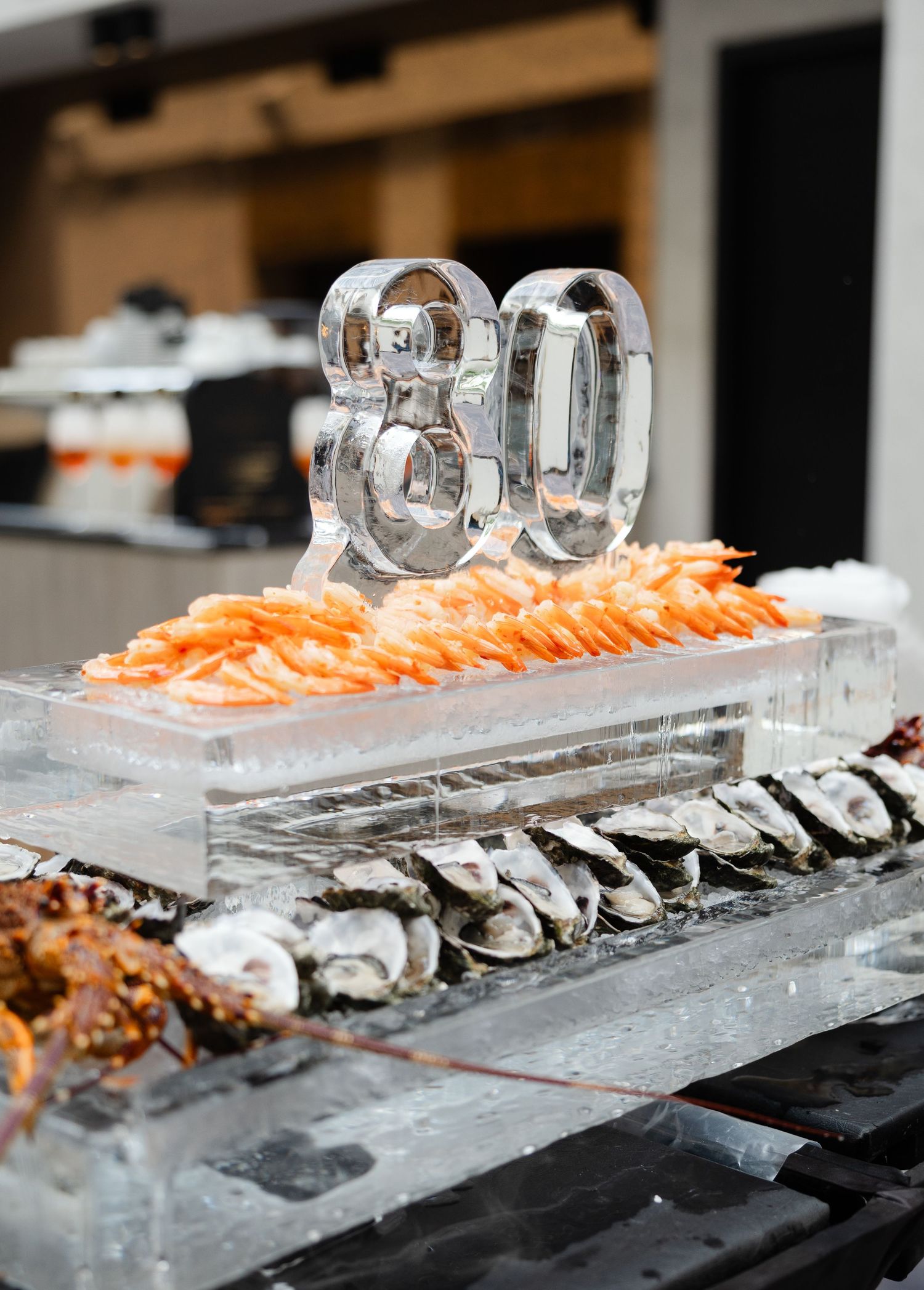 Raw oysters and shrimp artfully displayed on a long ice sculpture with illuminated numbers at a luxury event.
