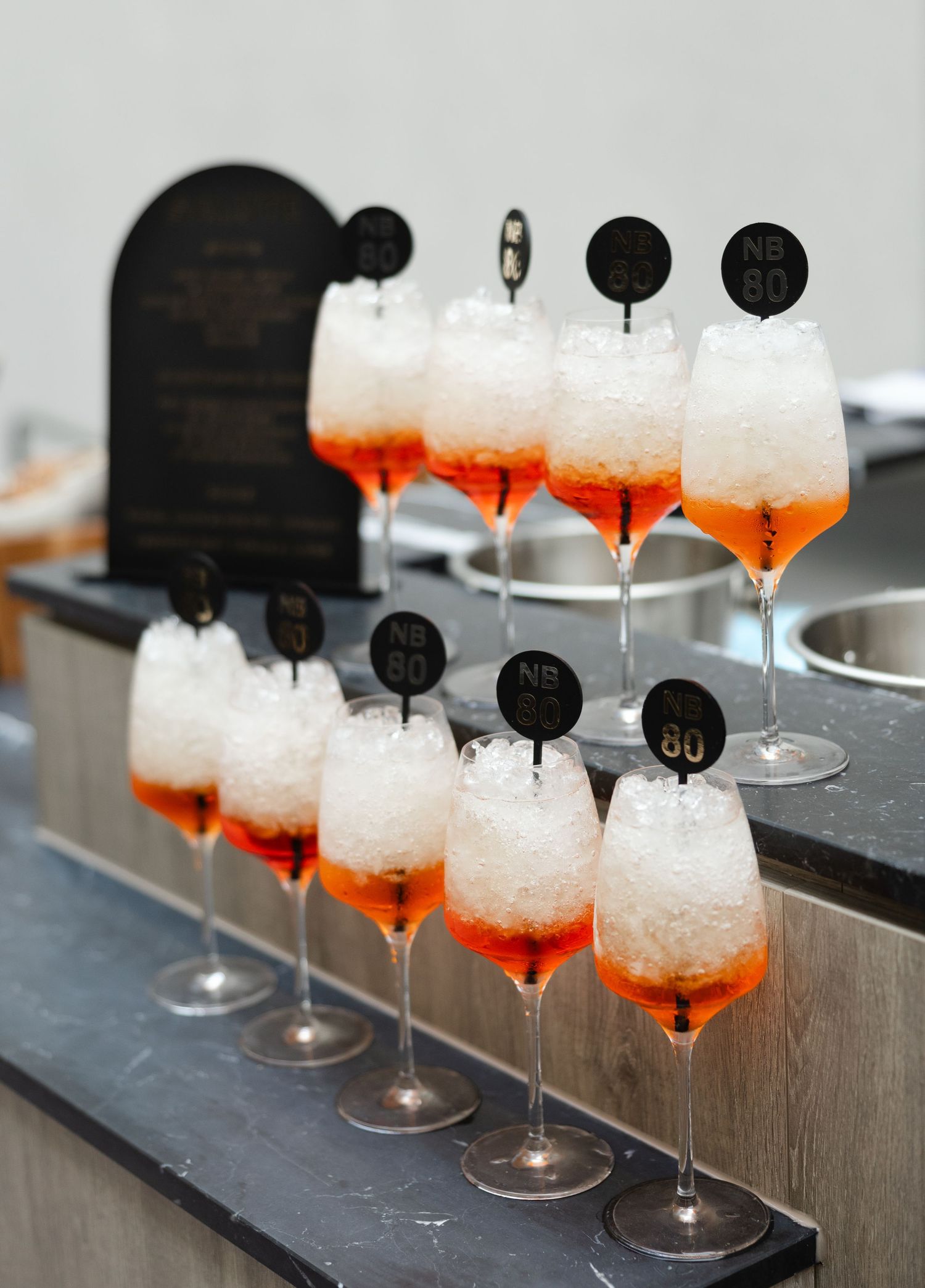 Row of tall cocktail glasses with orange liquor and crushed ice garnishes arranged on a dark wooden surface.