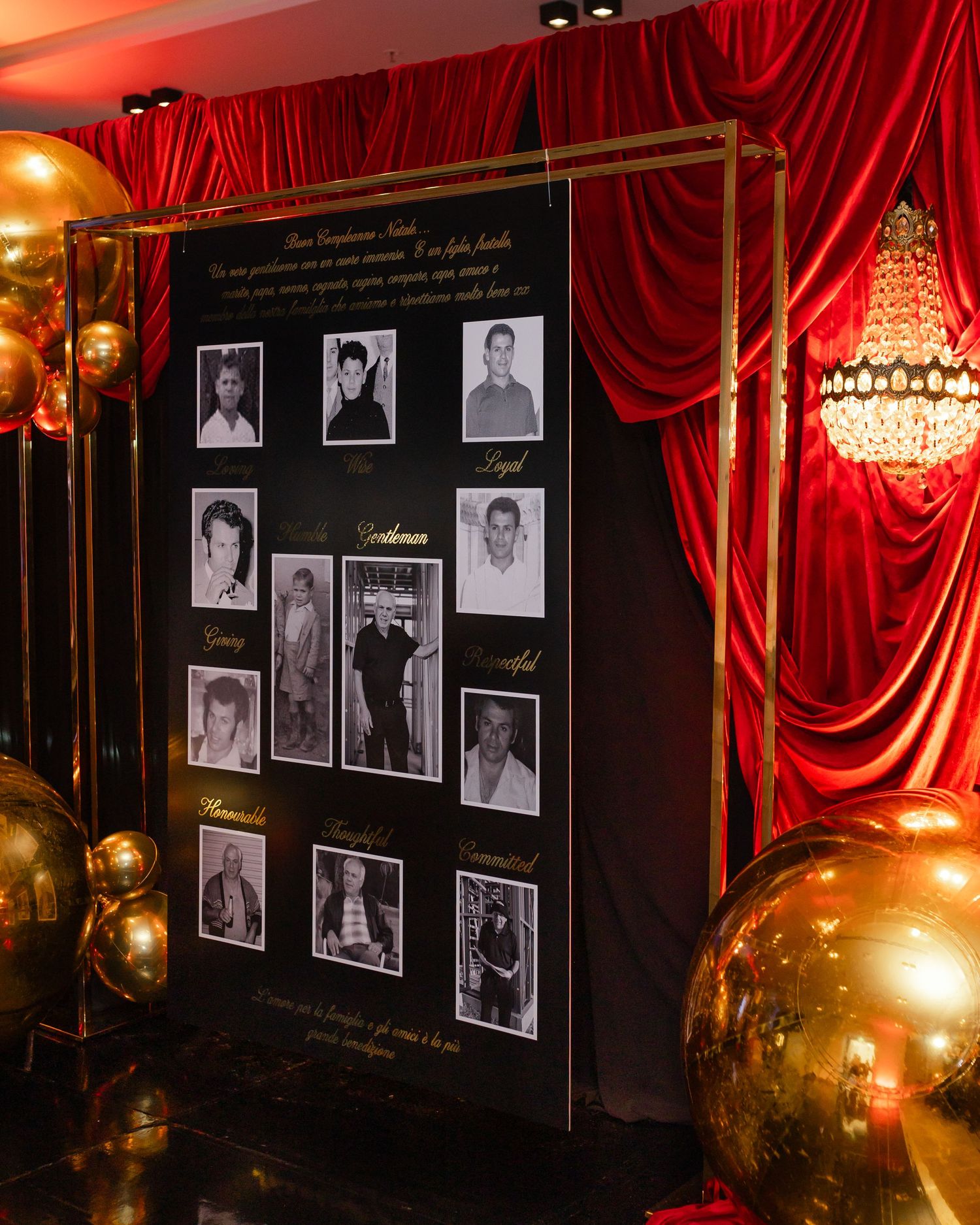 Vintage-style display with black and white photographs against dark wall, framed by red velvet curtains and crystal chandelier.