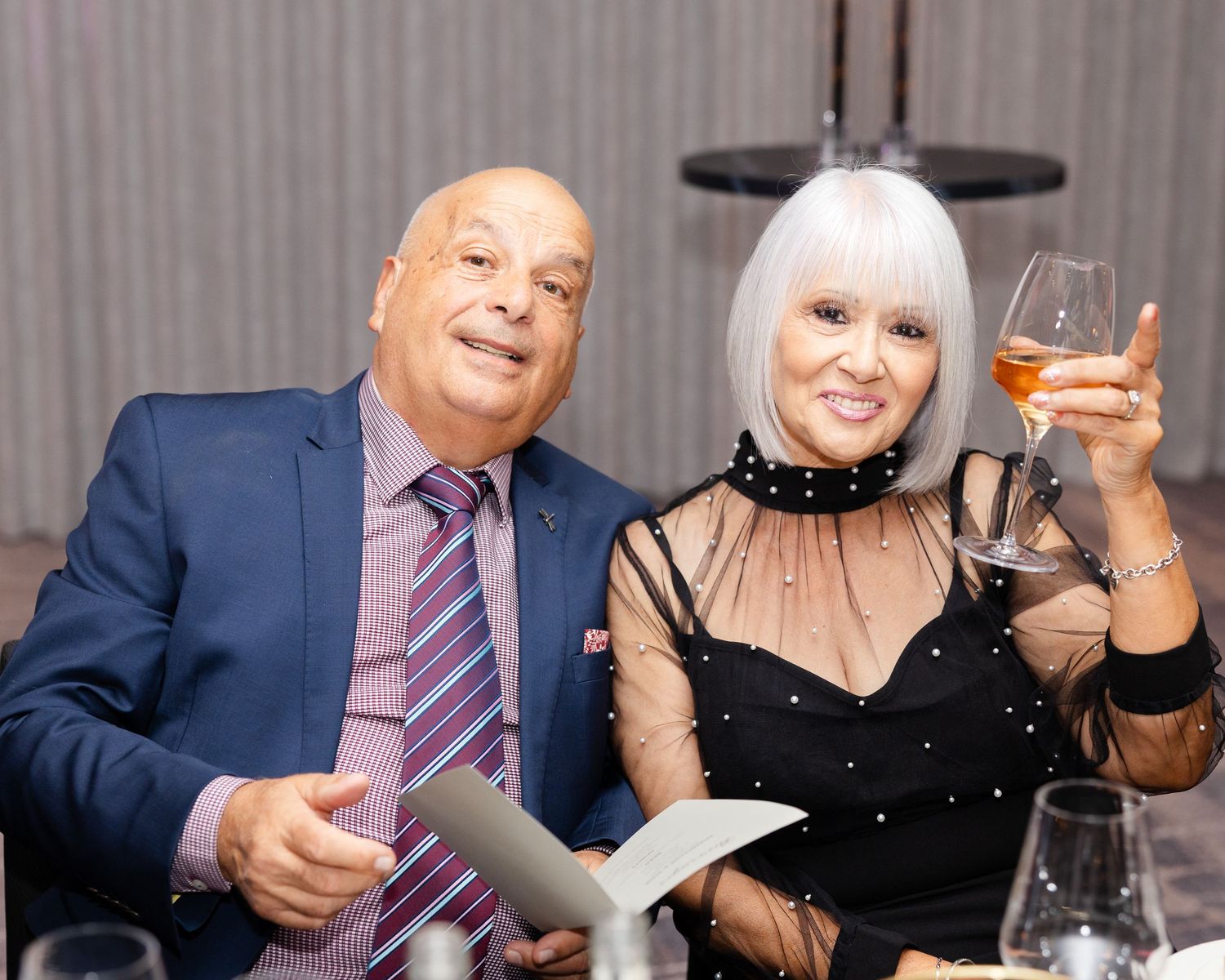 Two elegant party guests enjoying drinks and conversation at a formal dining event.