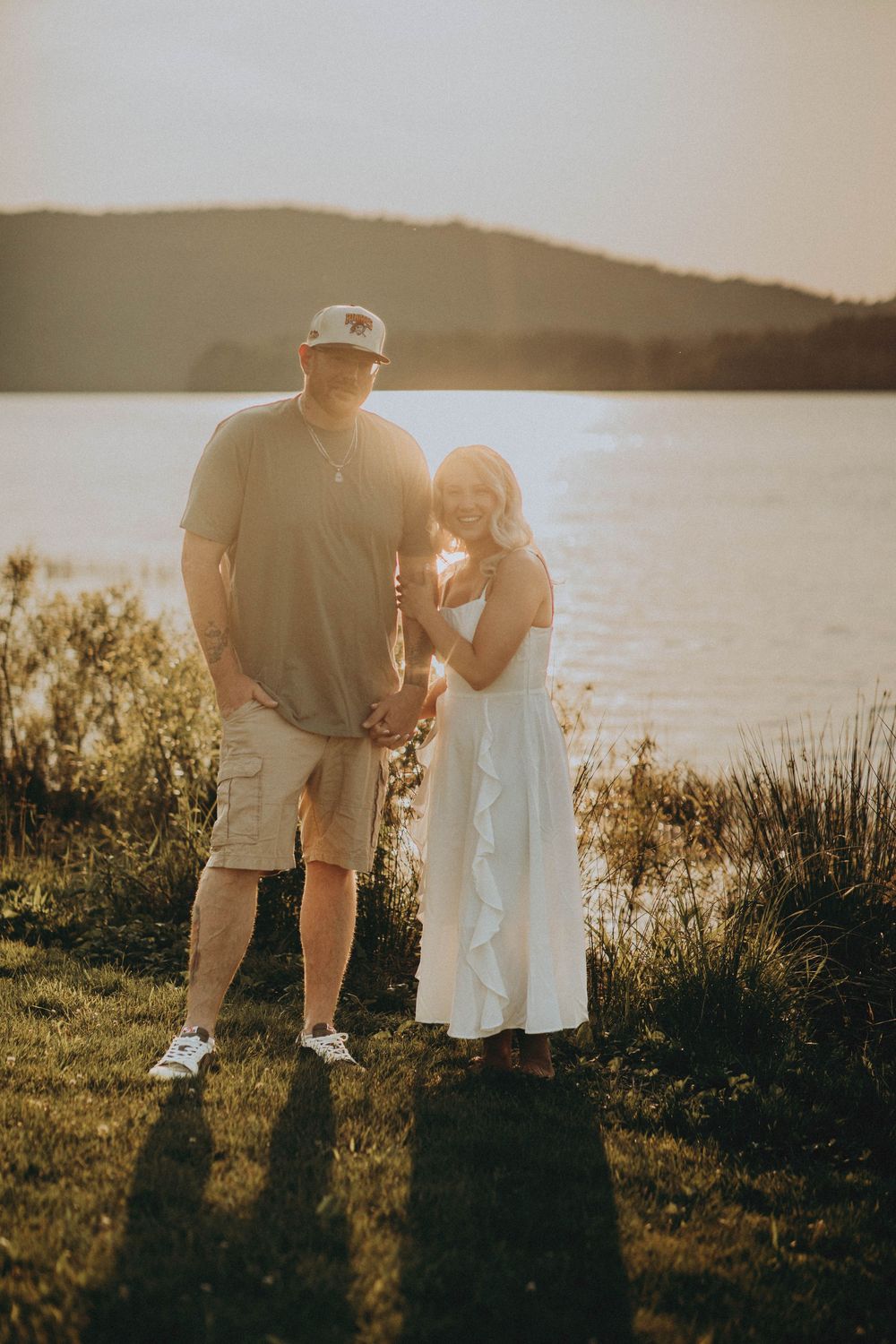 A couple stands together by a serene lake at sunset, surrounded by nature and warm golden light. indiana pa photographer yellow creek