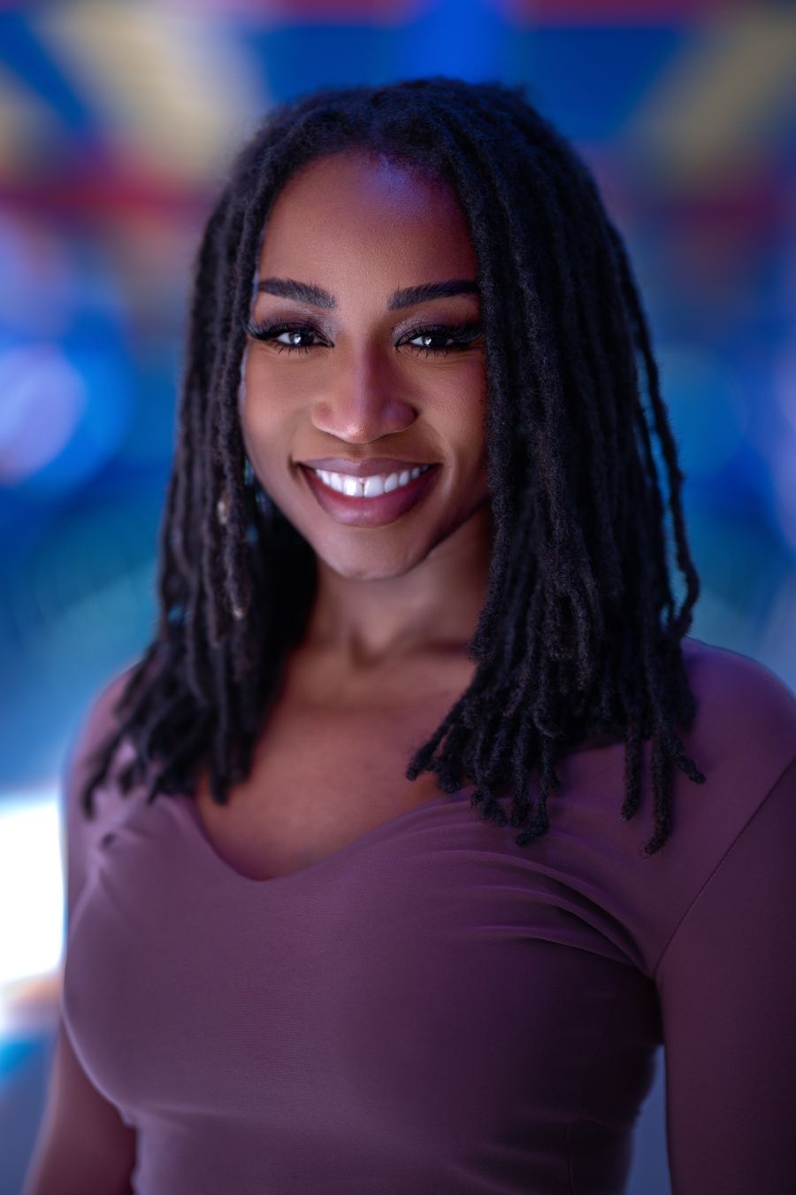 Person in dark purple top poses for series of portraits with colorful blue background lighting.