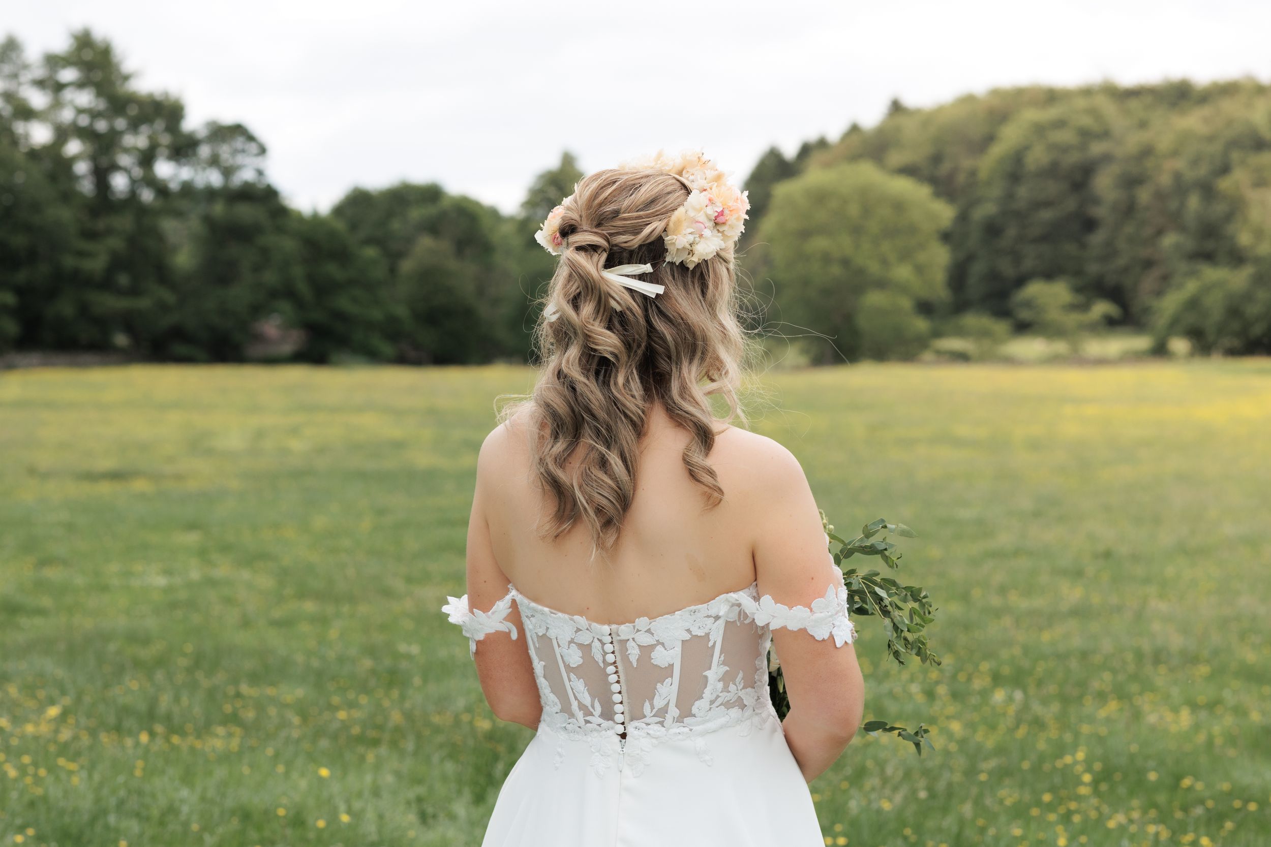 Back view of a bride in a lace corset dress standing in a green meadow.