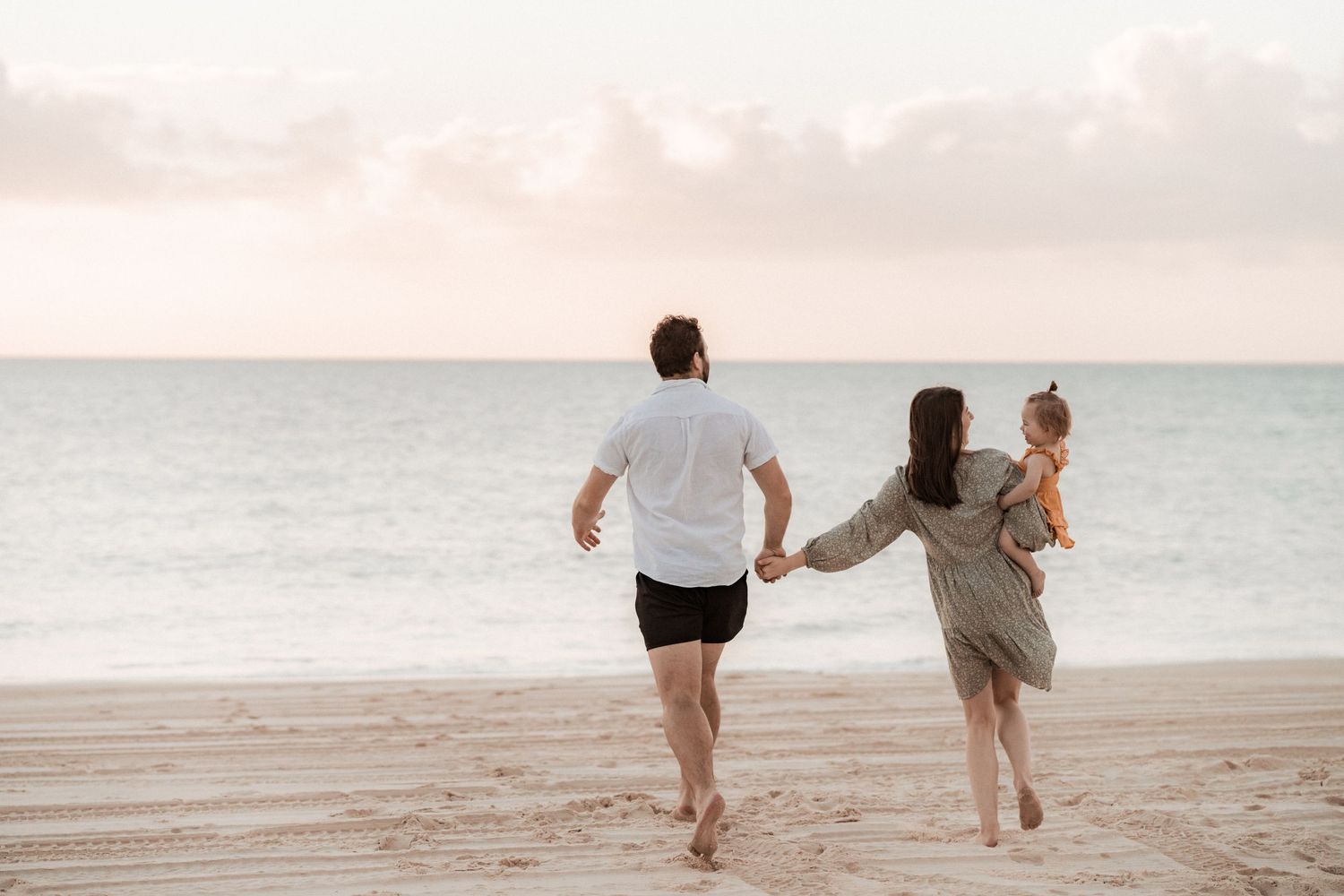 People holding hands while walking along a misty beach at sunset create a romantic silhouette against the ocean at Fraser Island / K'gari
