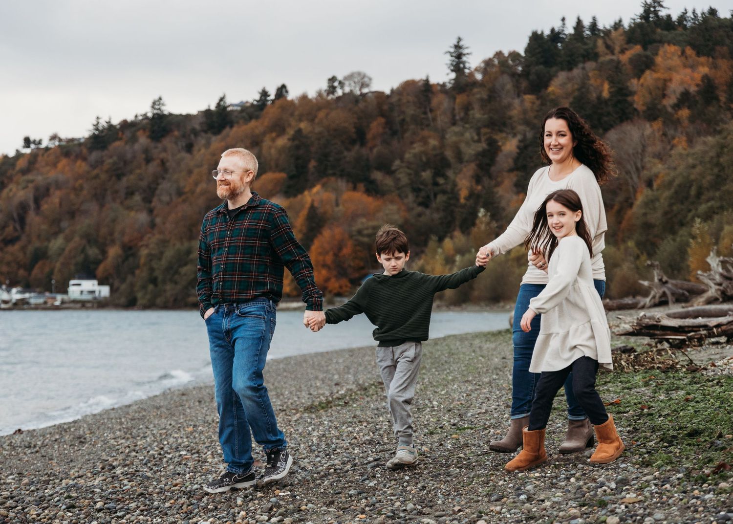 A family walks along a rocky beach shoreline surrounded by autumn trees and hillsides during golden hour.