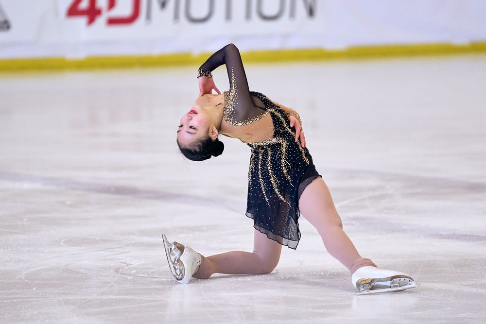 Figure skater in navy beaded dress performs graceful pose while kneeling on the ice during competition.