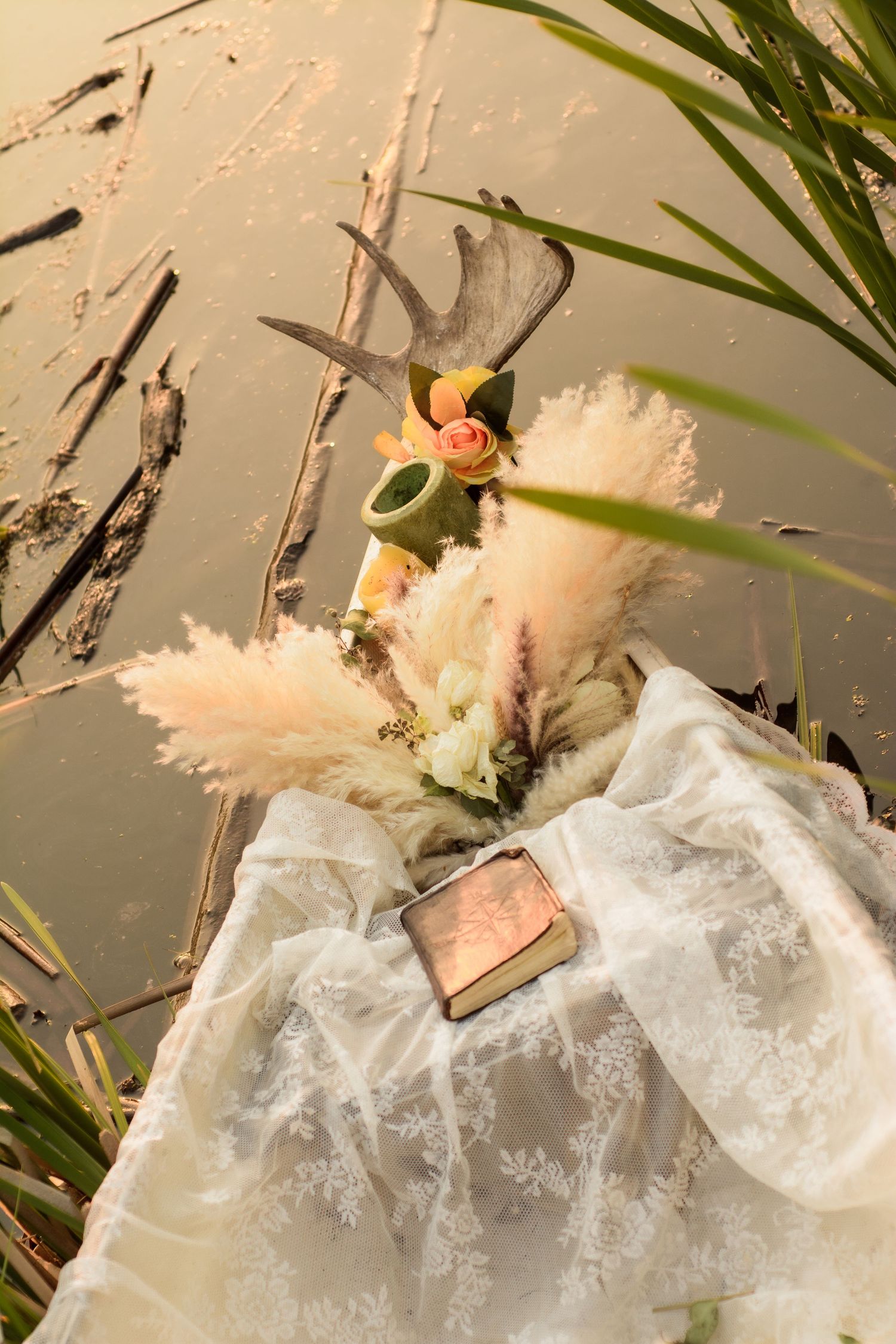 A vintage-style Christmas ornament with a delicate lace dress and white feathers hanging among green palm leaves.
