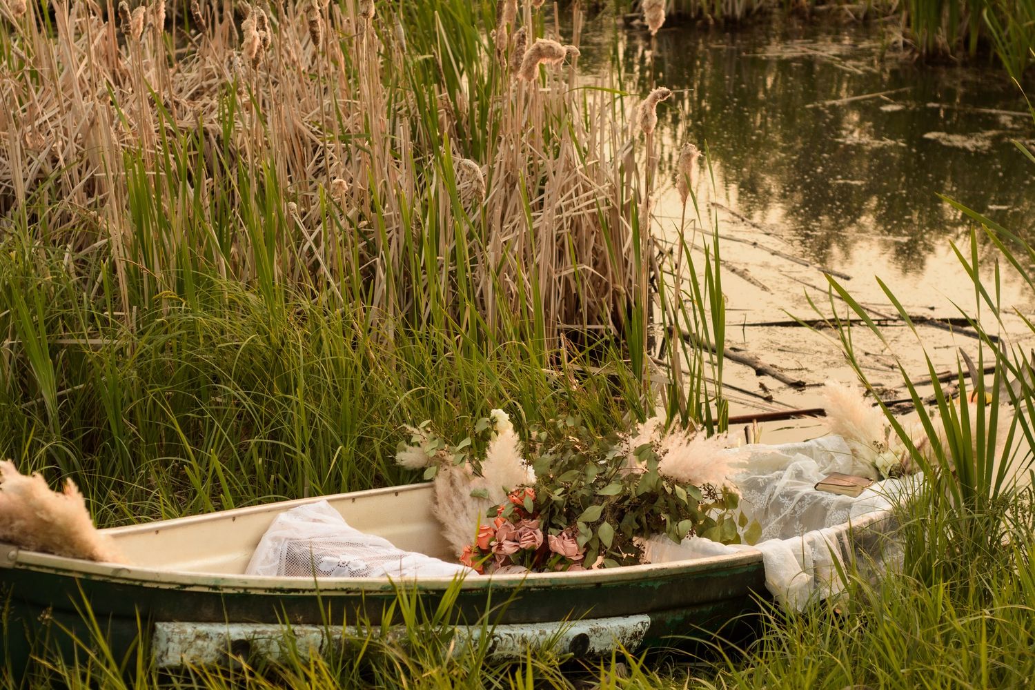 A person lies relaxing in an outdoor bathtub surrounded by tall reeds and marsh grasses beside a pond.