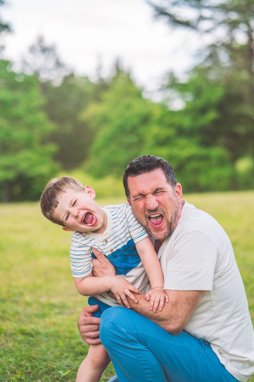Candid moment of laughter and play between parent and child outdoors in a green field.