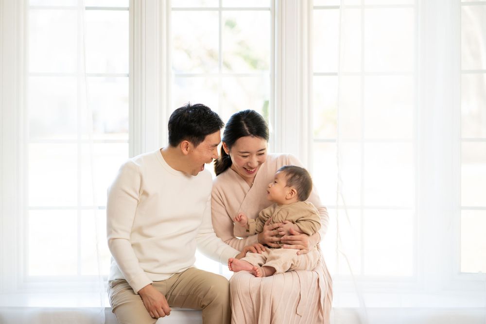 Family sharing tender moment together in bright sunlit room with white windows.