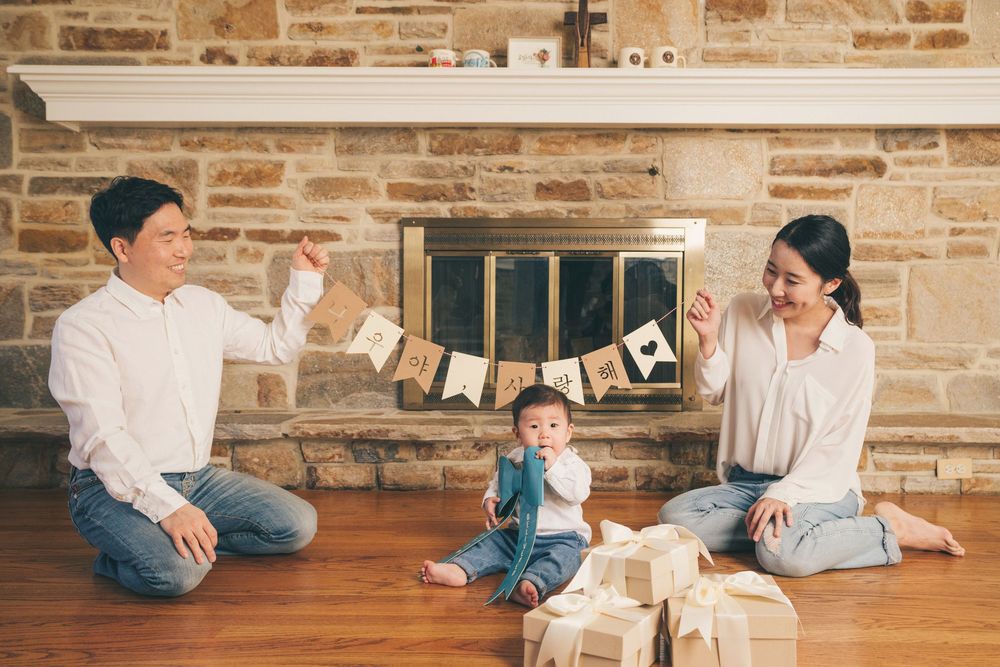 A family celebrates with wrapped gifts and decorations in front of a stone fireplace.