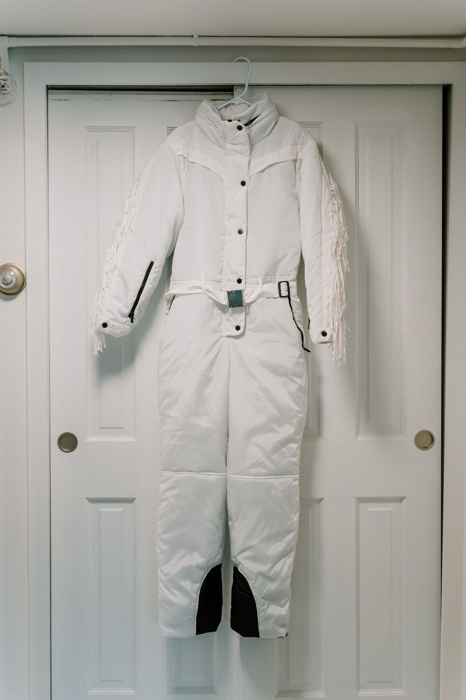 White winter ski bibs and coats displayed on white doors showing winter outerwear collection.