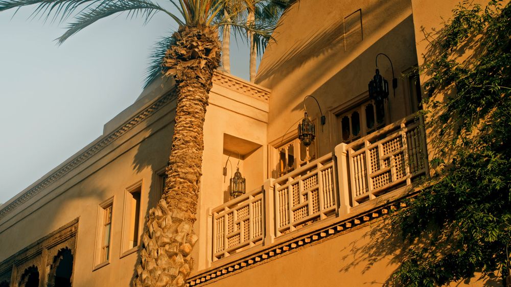 Panoramic view of a Mediterranean-style mansion exterior with palm trees at golden hour.