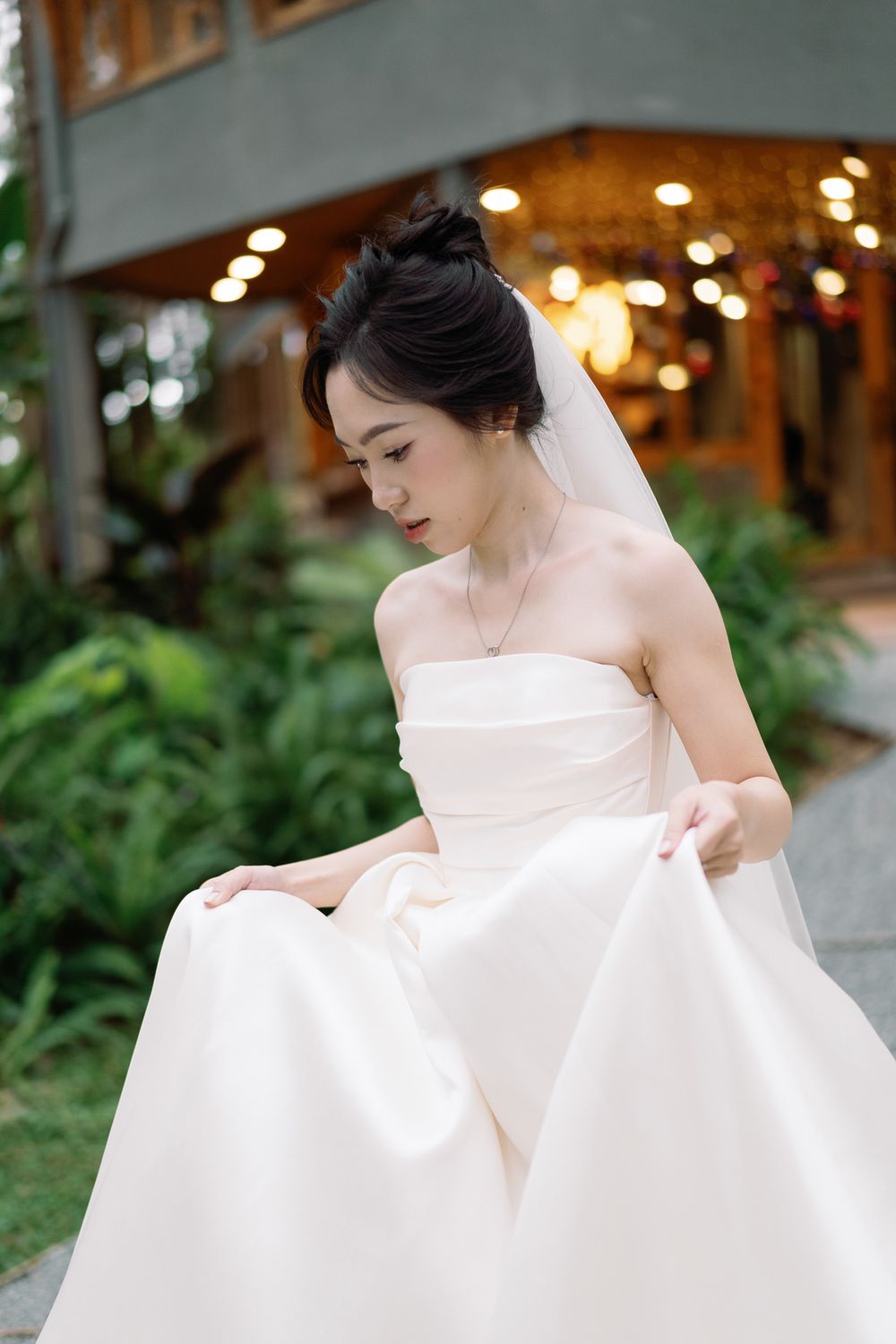 Bride in classic white strapless ballgown with veil poses outdoors near garden.
