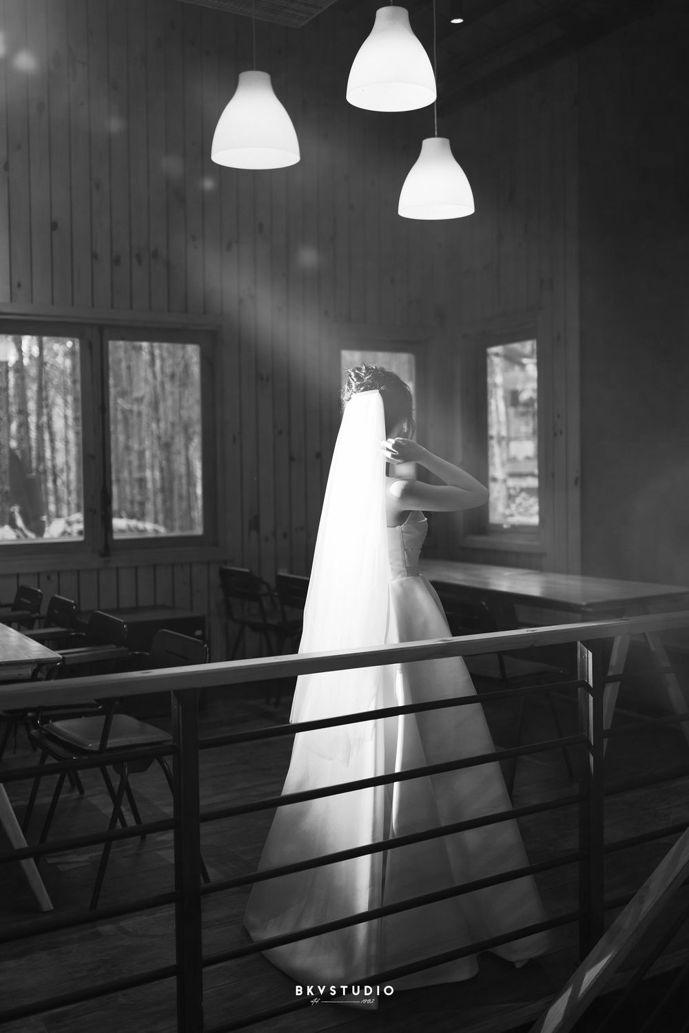 Dramatic black and white photo of a wedding dress silhouette against pendant lights and windows.