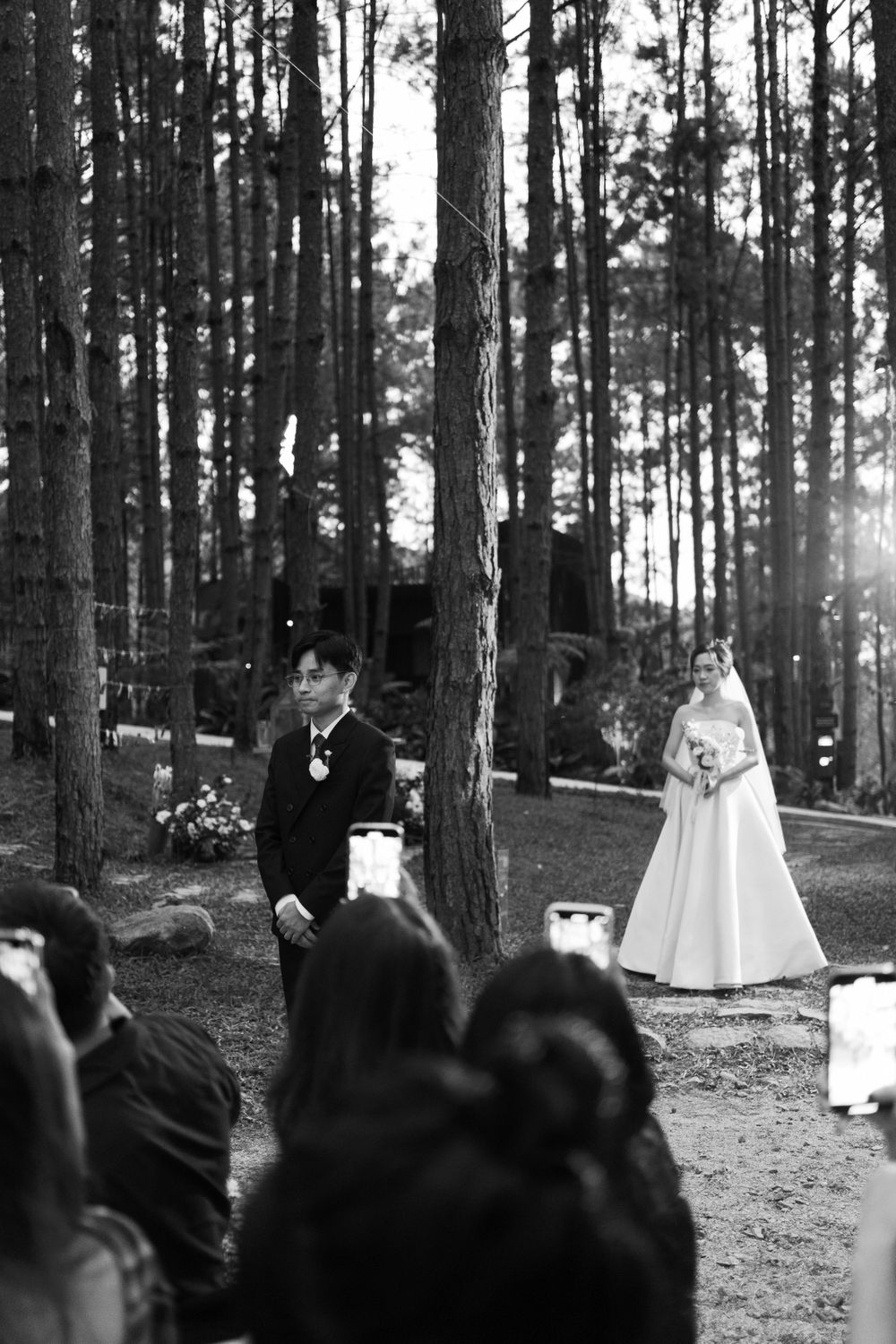 Black and white outdoor wedding ceremony in a pine forest with guests watching.