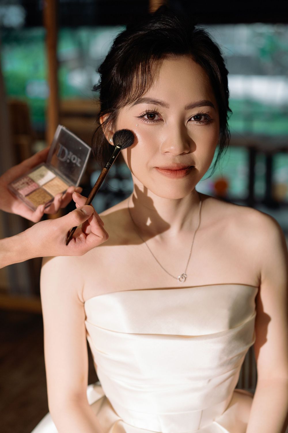 Behind-the-scenes of bridal makeup application in warm natural light.