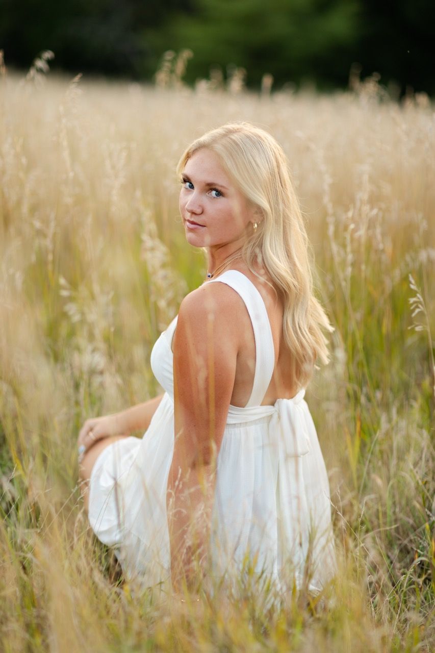 Dreamy outdoor portrait in a flowing white dress amid tall golden grass.